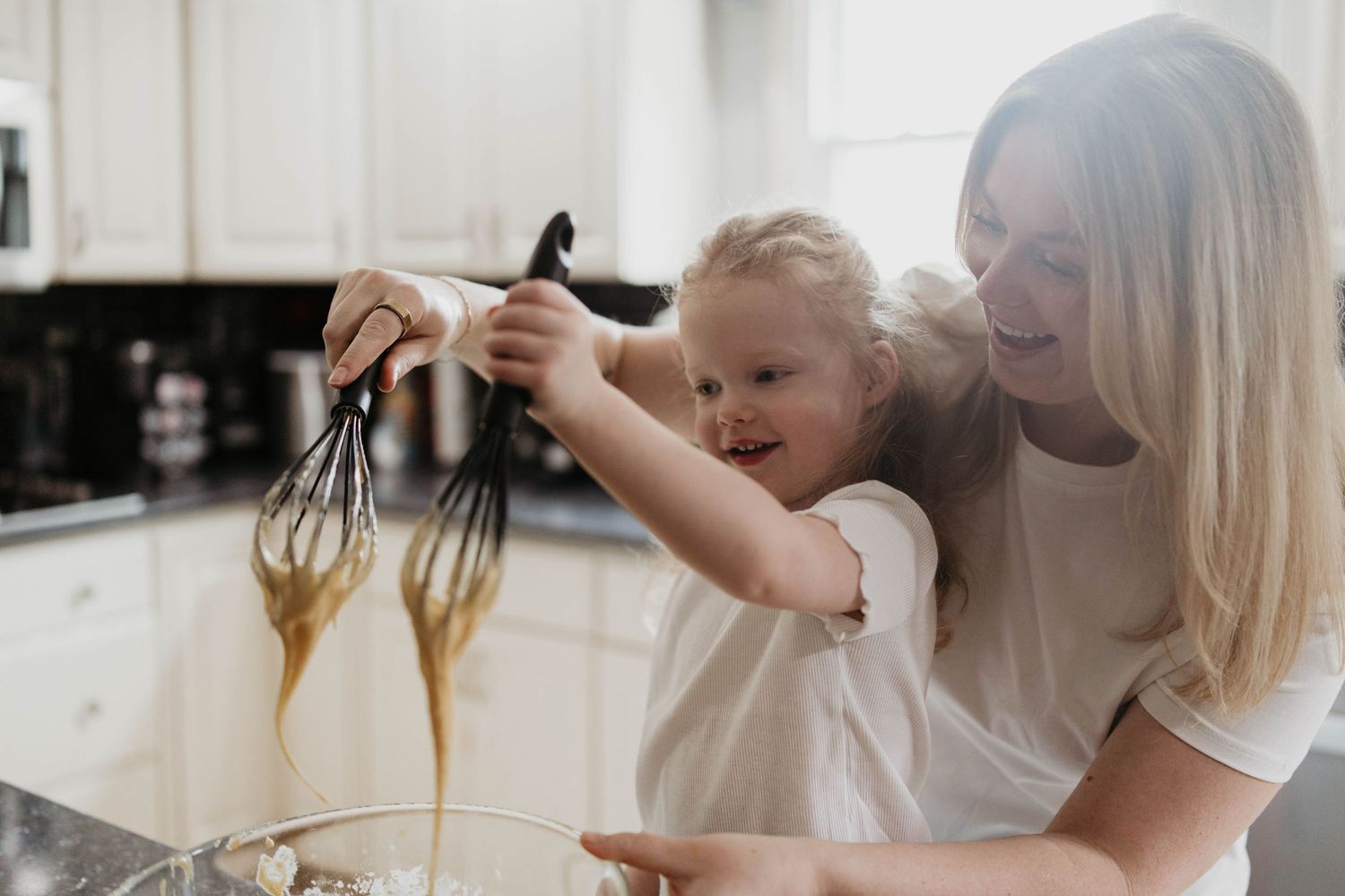 A parent and child baking together in a kitchen, mixing chocolate batter with handheld beaters.