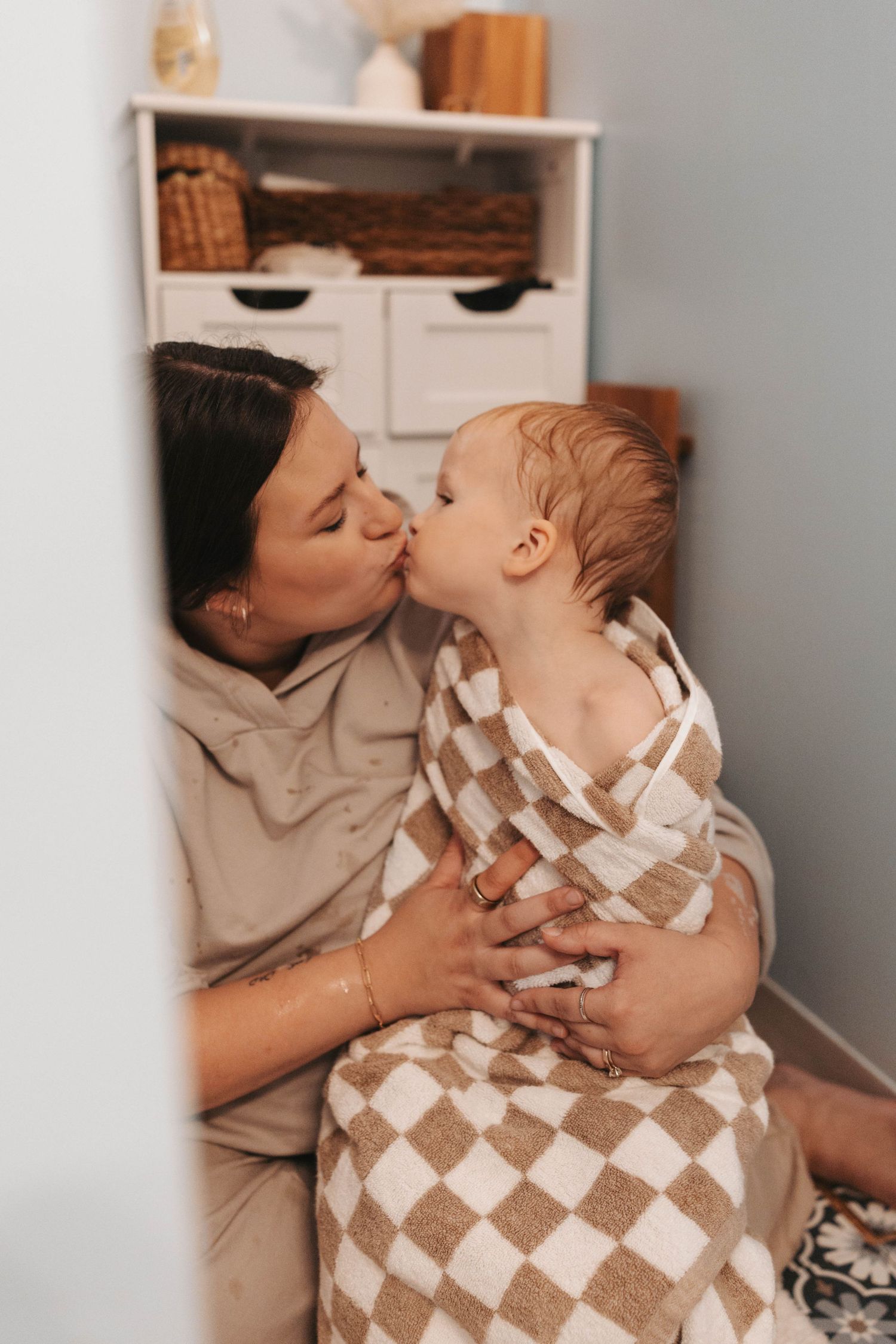 Parent and child sharing tender moment while wrapped in checkered brown and white towel after bath.