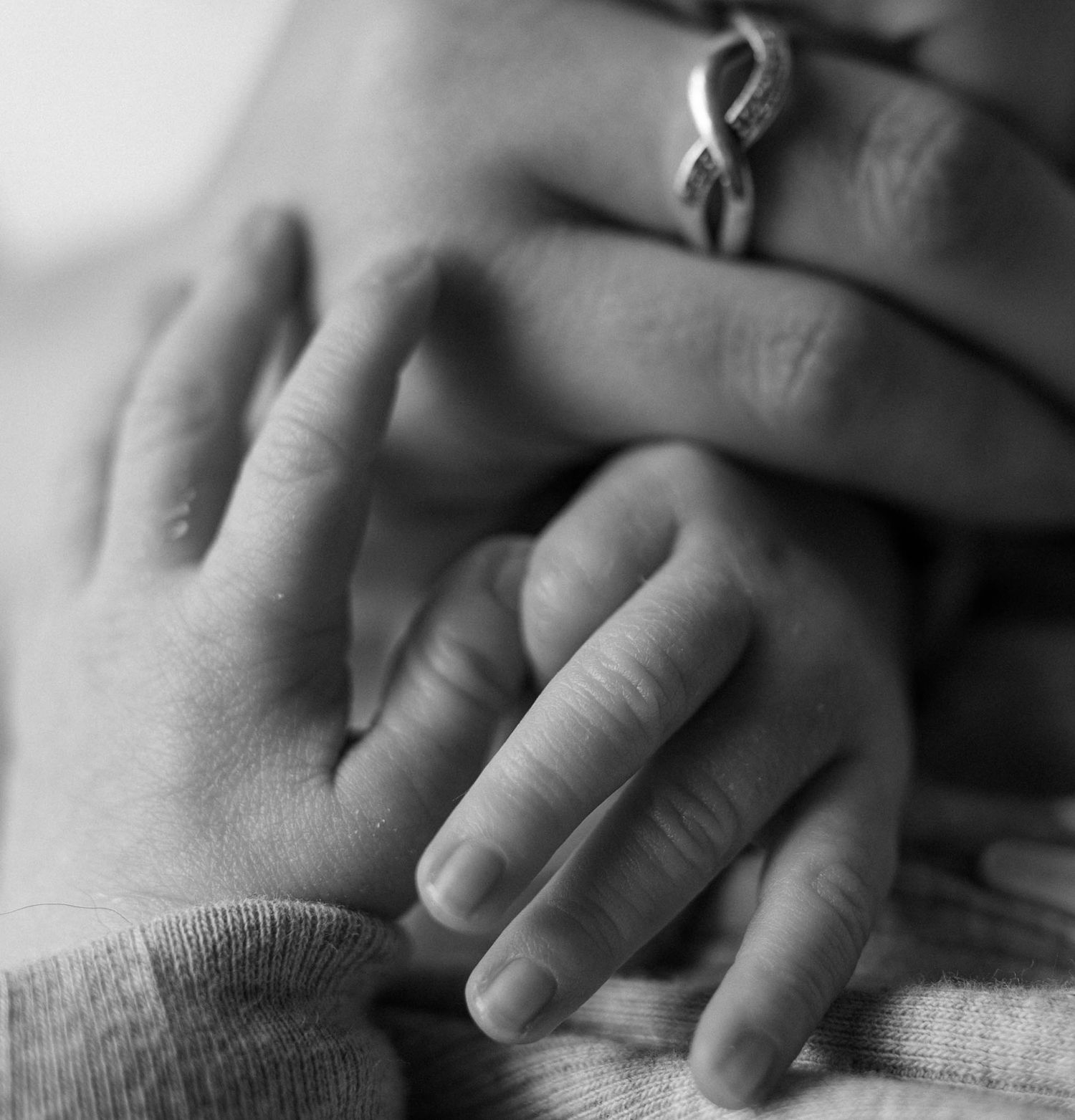 Black and white photo of a newborn baby's tiny hand resting on an adult's hand wearing a ring.