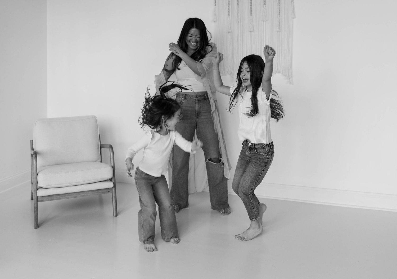 Black and white photo of a mother dancing joyfully with her three children in a bright white room.