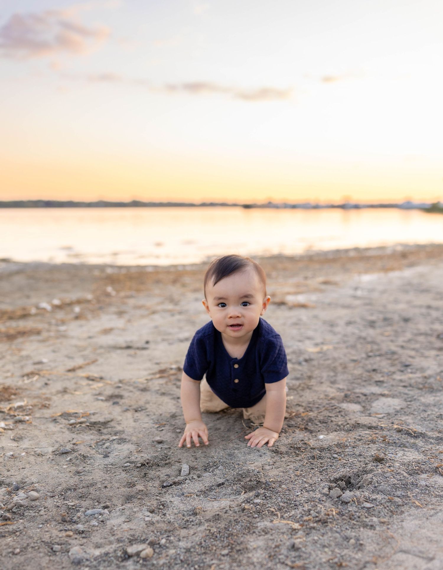 Small child crawling on sandy beach at sunset with golden light illuminating the peaceful coastal scene.