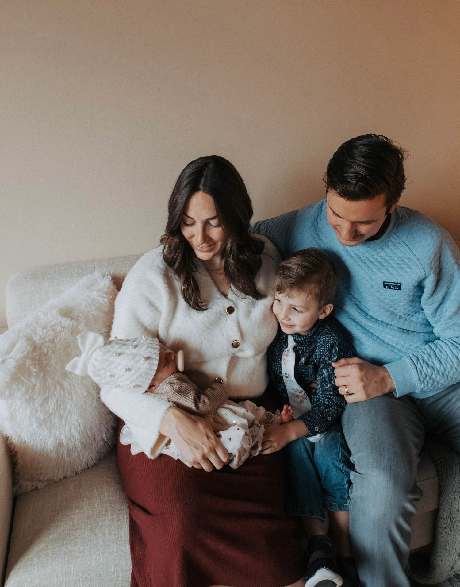 Family sits together on couch sharing intimate moment while holding and gazing at newborn baby.