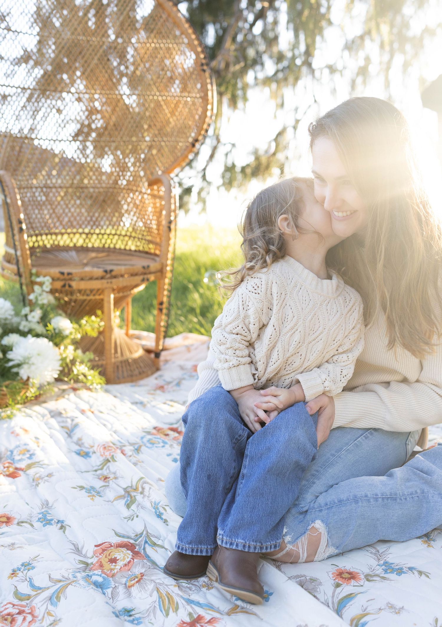 A tender moment on a floral blanket with wicker peacock chair and sun flare glowing in the garden backdrop.