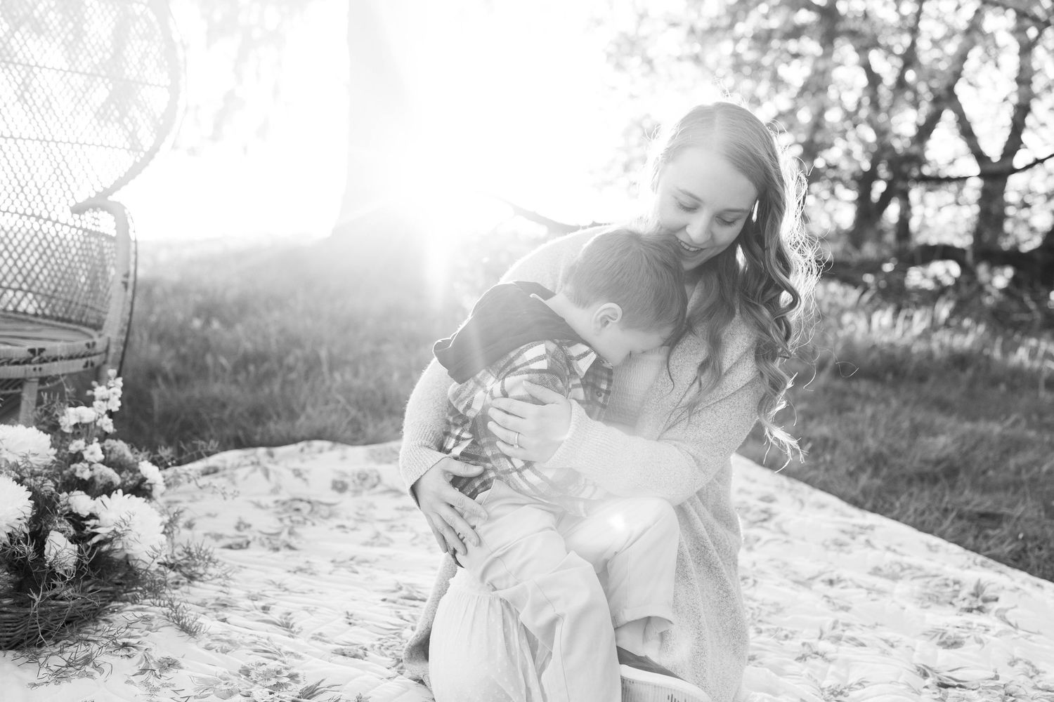 A heartwarming black and white photo capturing a tender embrace in a sun-drenched outdoor setting with a blanket.