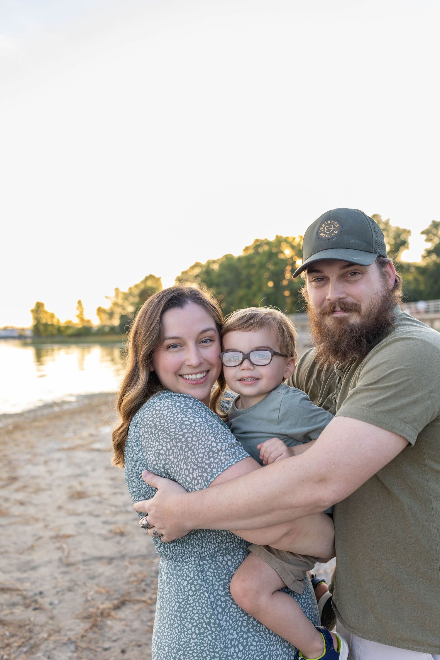 Family shares joyful embrace on a beach during golden hour with trees visible in background.