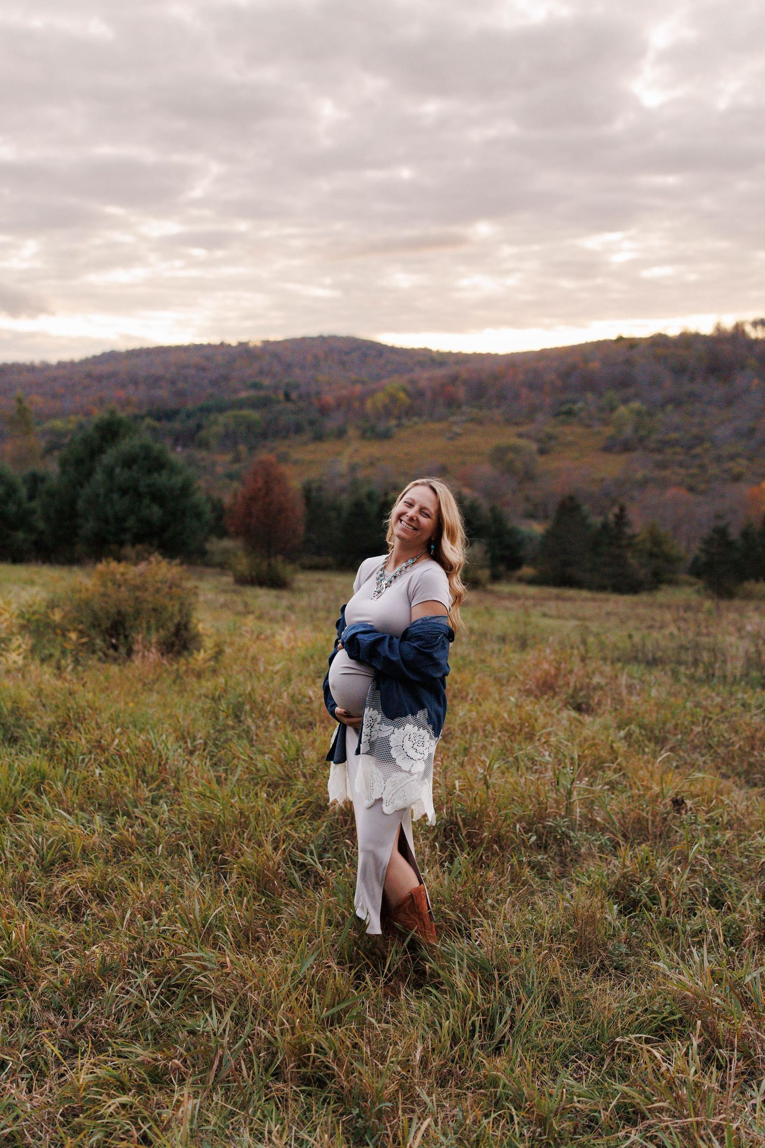 A couple embraces in a scenic autumn meadow with rolling hills and fall foliage in the background.