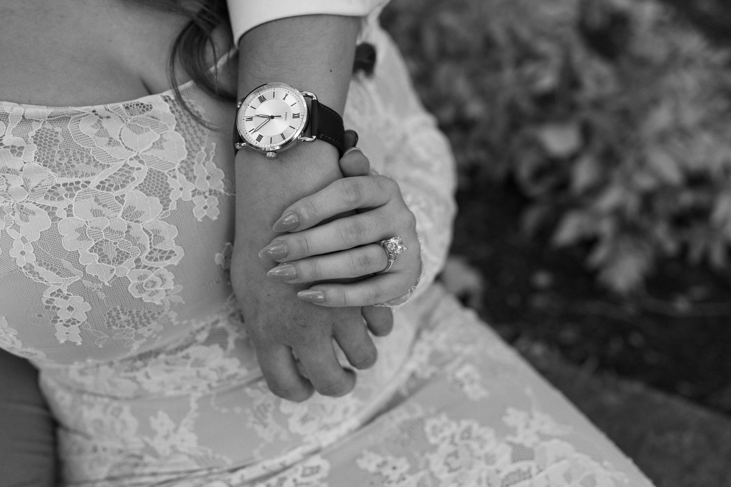 A close-up shot of hands resting on white lace wedding dress fabric.
