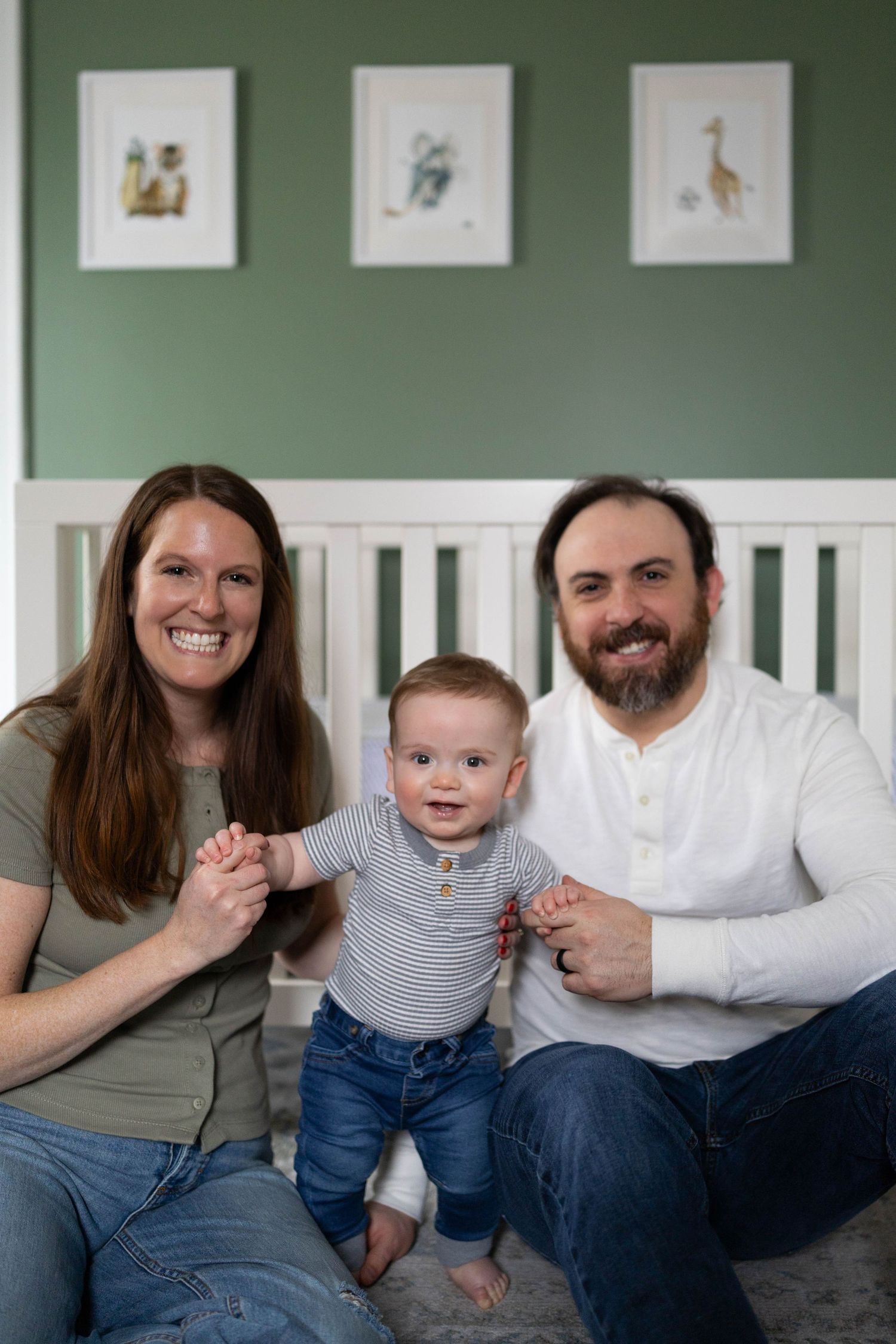 Family sitting together on couch with nursery artwork featuring animals displayed on sage green wall above them.