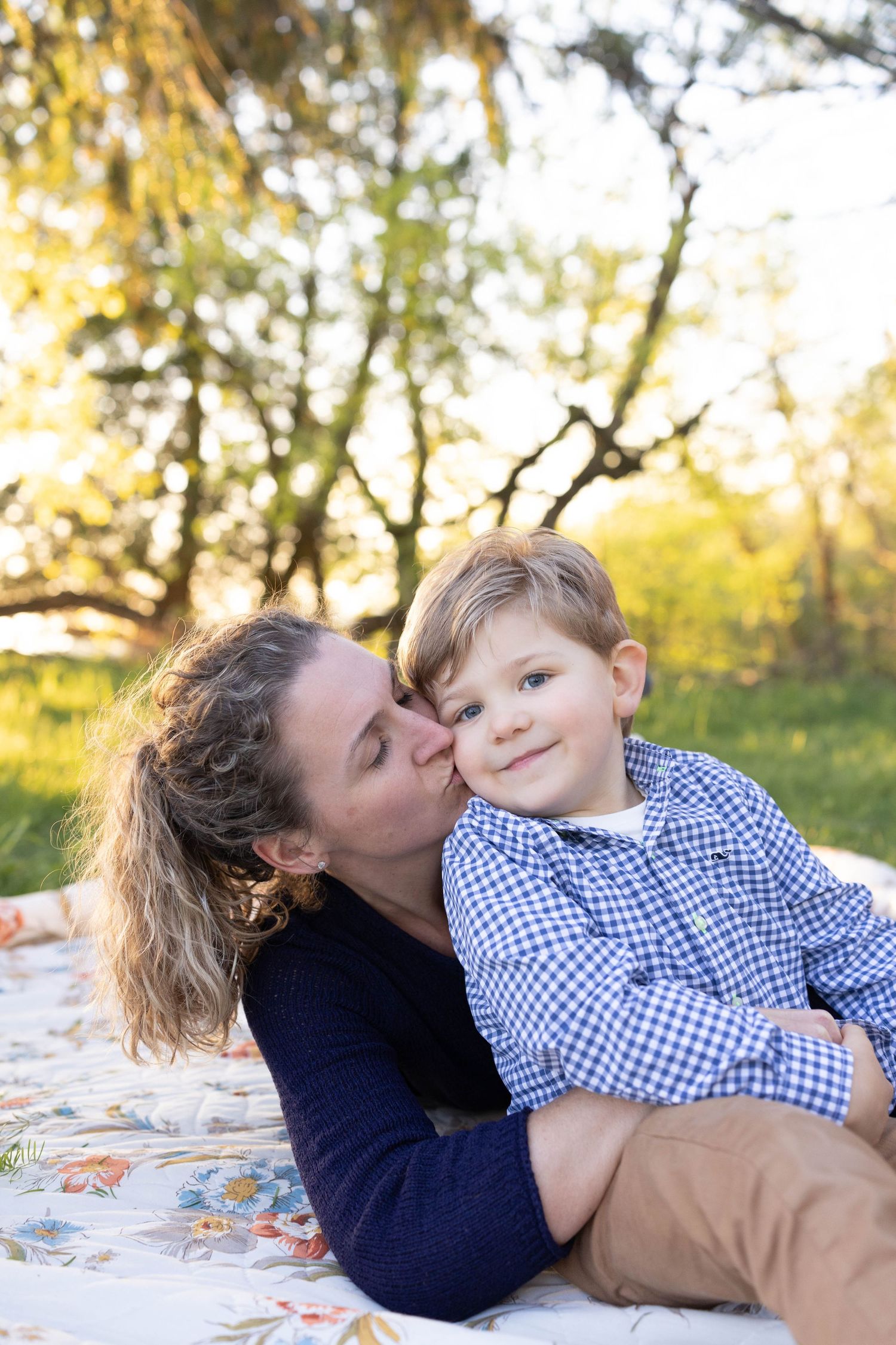 Sweet outdoor photo of a tender moment between mother and child sitting on a floral blanket in warm sunlit setting.