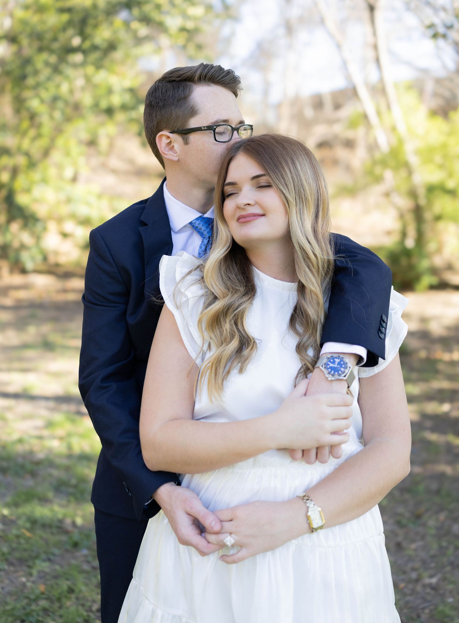 A tender wedding portrait of a couple embracing outdoors in a park setting, with soft natural lighting and greenery.