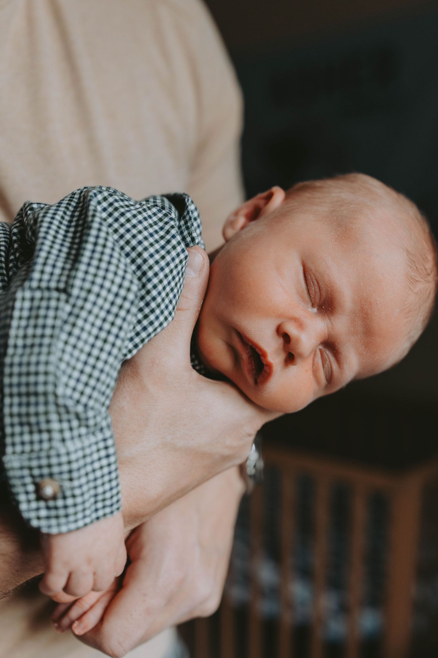 Newborn baby in checkered shirt sleeping peacefully in parent's arms.
