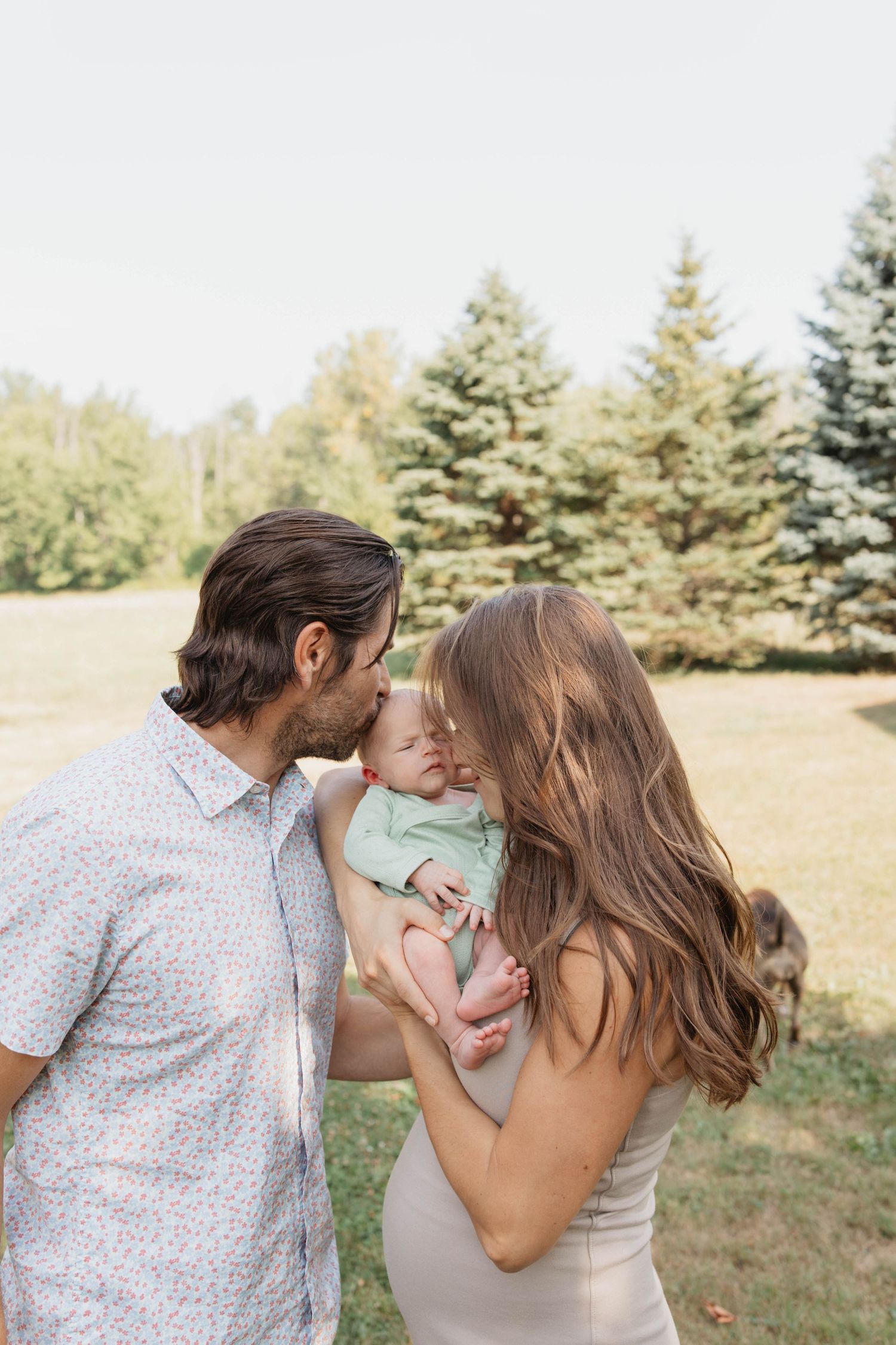 Family sharing tender moments together outdoors with evergreen trees in the background.