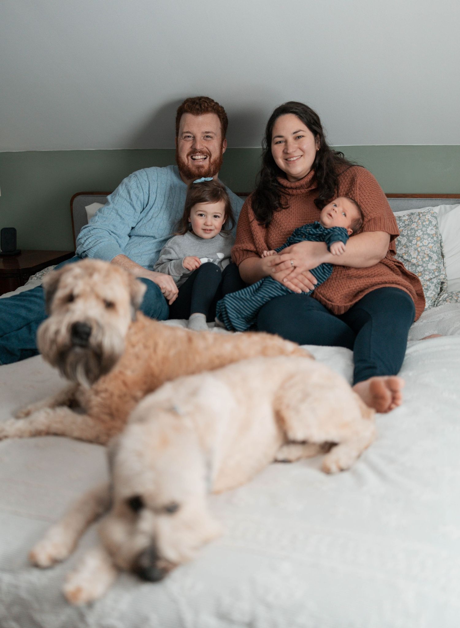 A family lounges together on a couch with their large dog, sharing a relaxed moment in casual attire.
