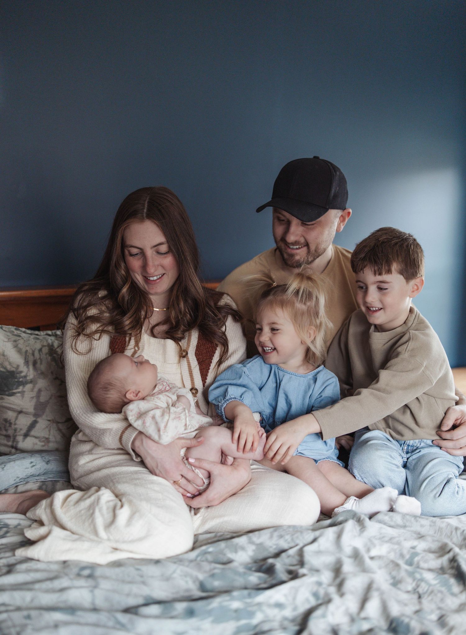 A family shares a cozy moment together on a bed, with everyone laughing and snuggling close.