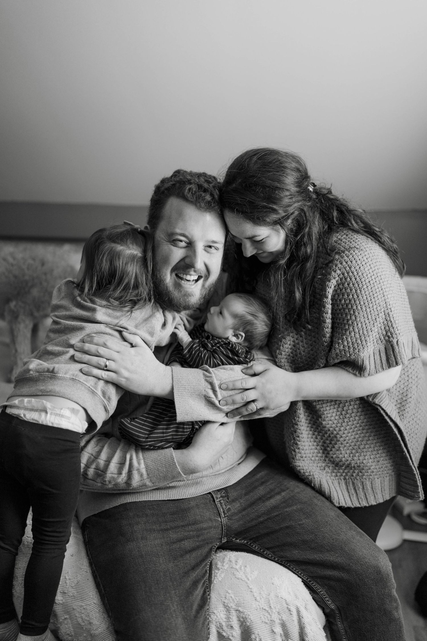 Black and white intimate family portrait showing tender moment of embrace and connection on a couch.