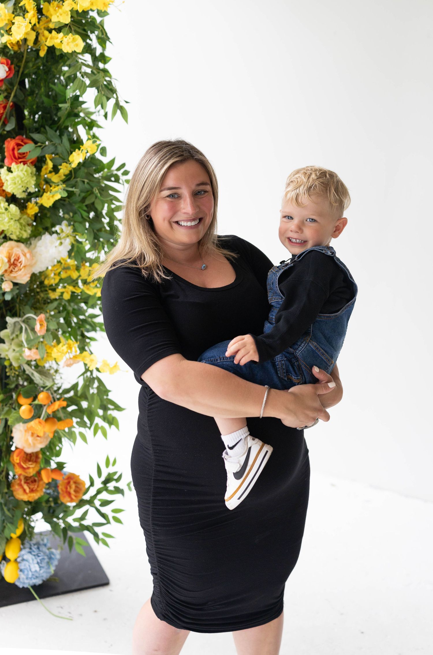 An endearing portrait of a parent and toddler posing together against a floral backdrop with yellow and orange blooms.