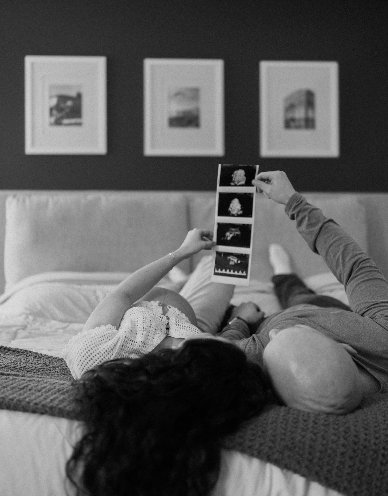 Someone lying down and looking at ultrasound photos while relaxing on a couch with framed artwork on the wall behind.