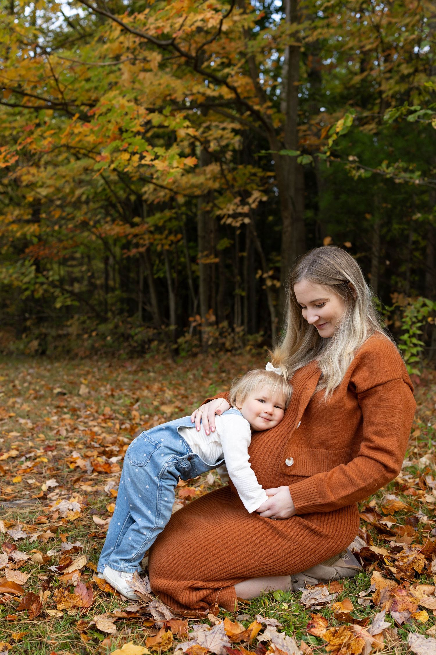 A tender autumn moment shared on fallen leaves in the woods, wearing a cozy rust-colored sweater dress.