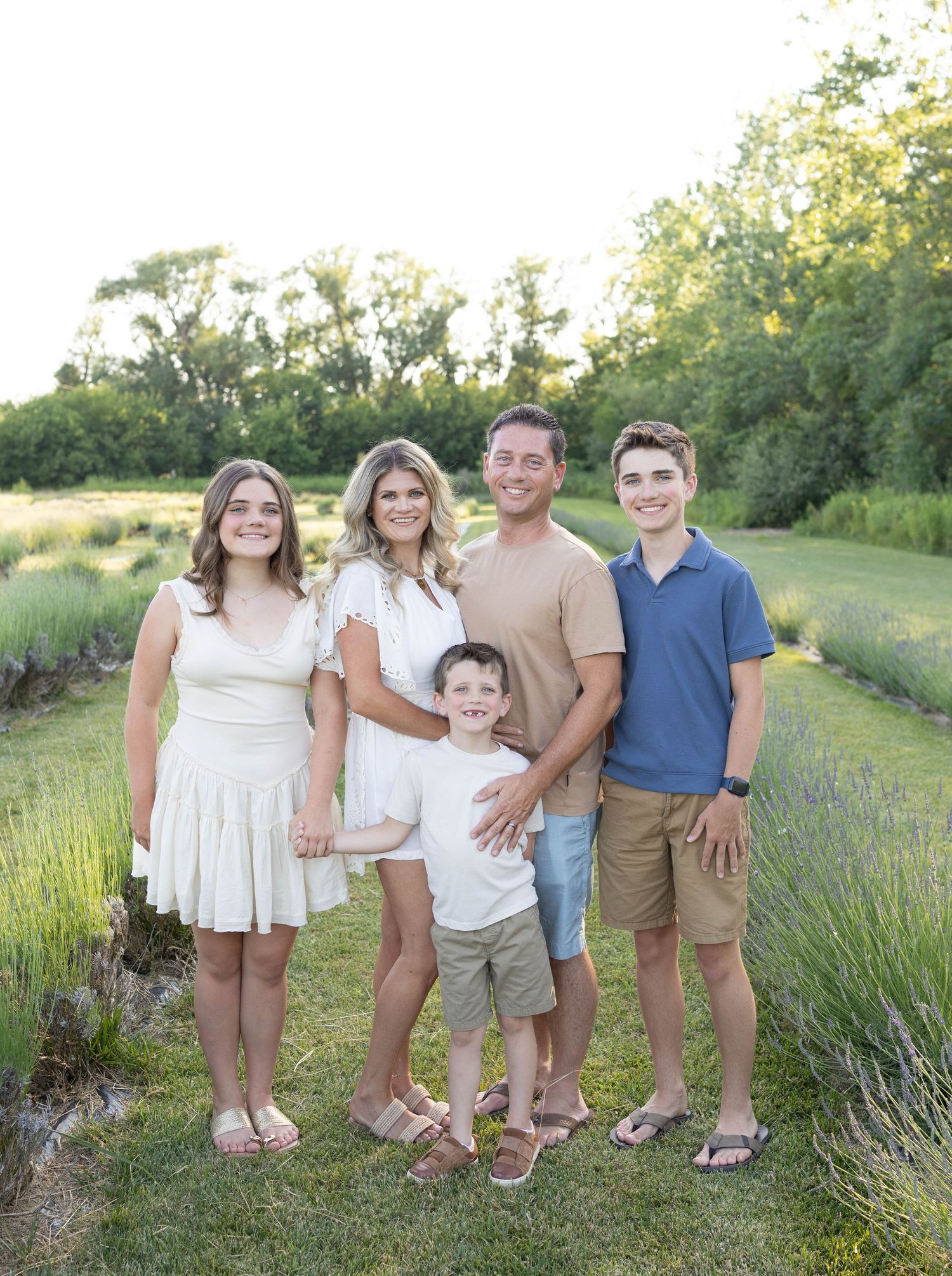 Family poses together in a lavender field during golden hour with trees and greenery in the background.