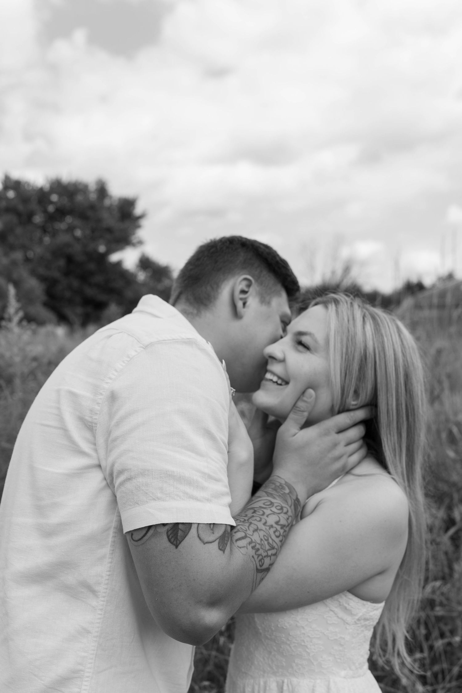 Black and white photo of a couple sharing a tender moment outdoors, man whispering to smiling woman.