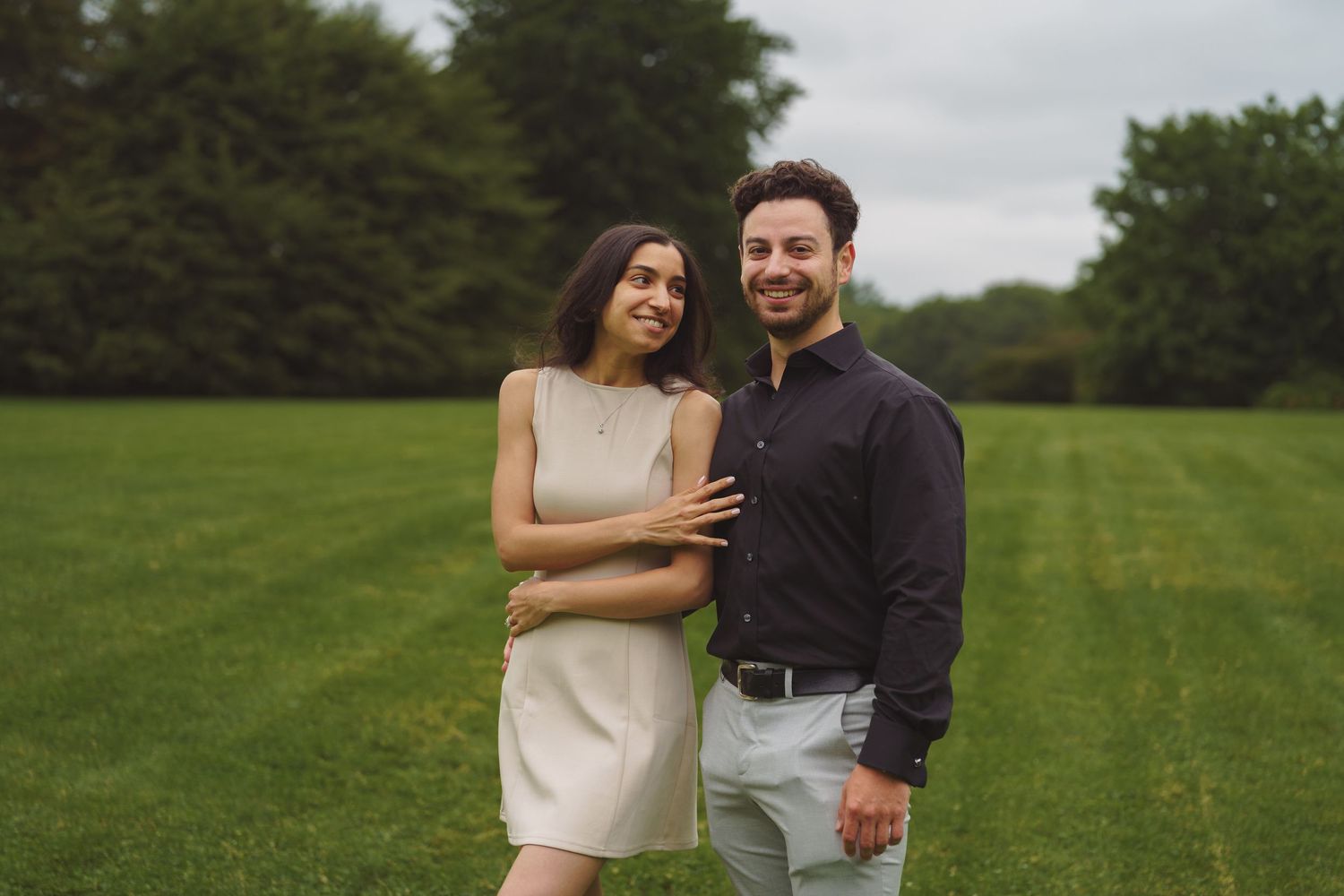 A couple shares a joyful moment together while standing on a green lawn with trees in the background.