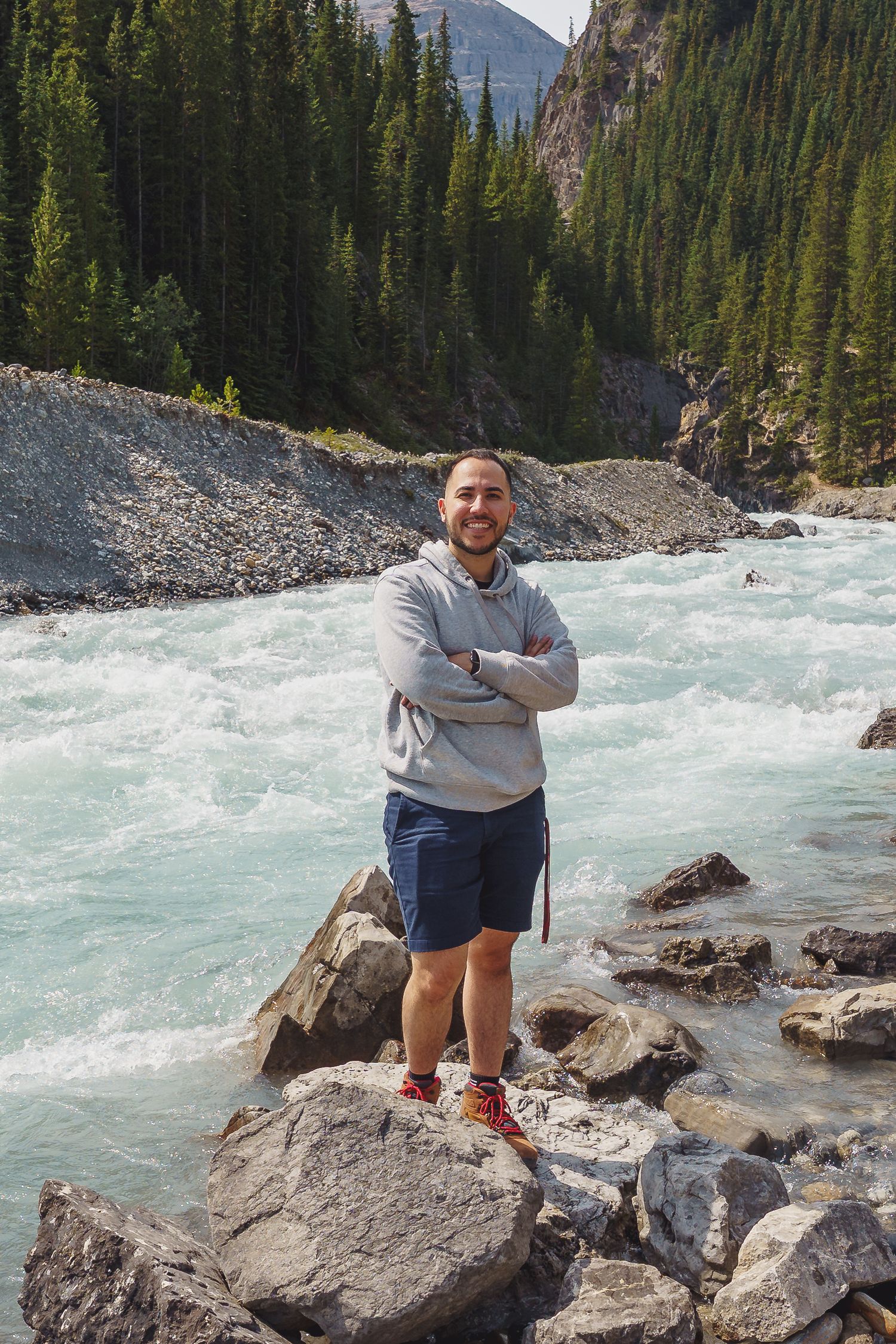 Scenic mountain river rushing past rocky outcrops with evergreen forest and peaks in the background.