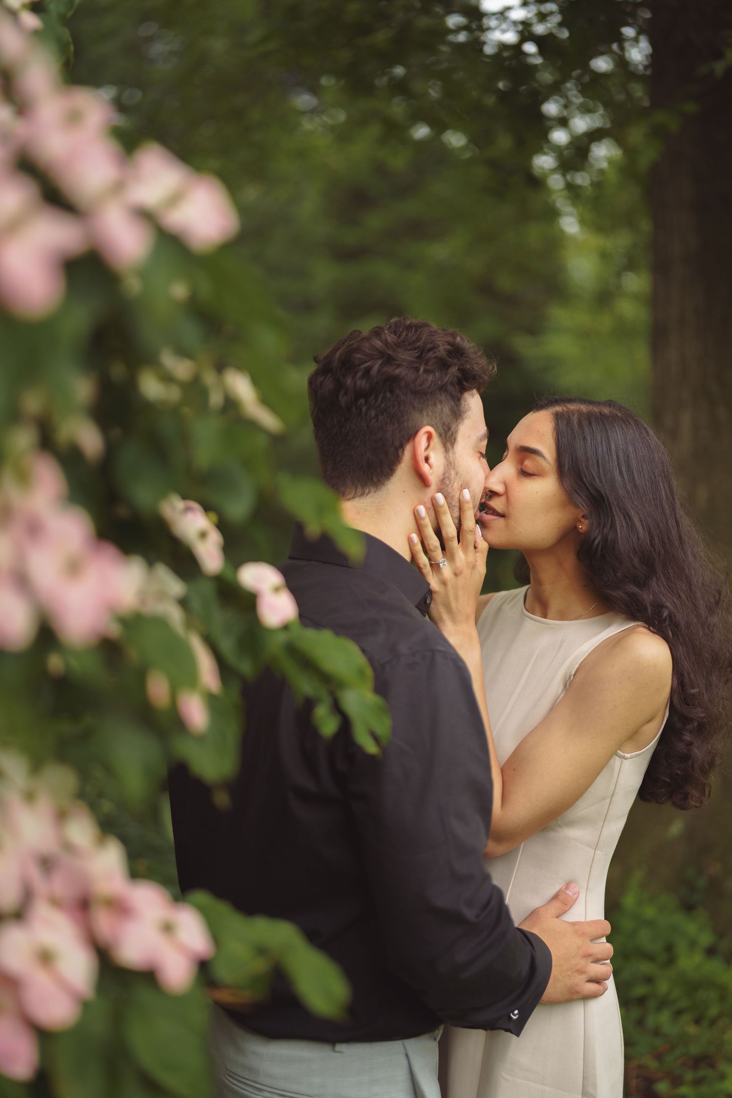 A tender romantic moment captured between a couple among blooming pink flowers in a garden setting.