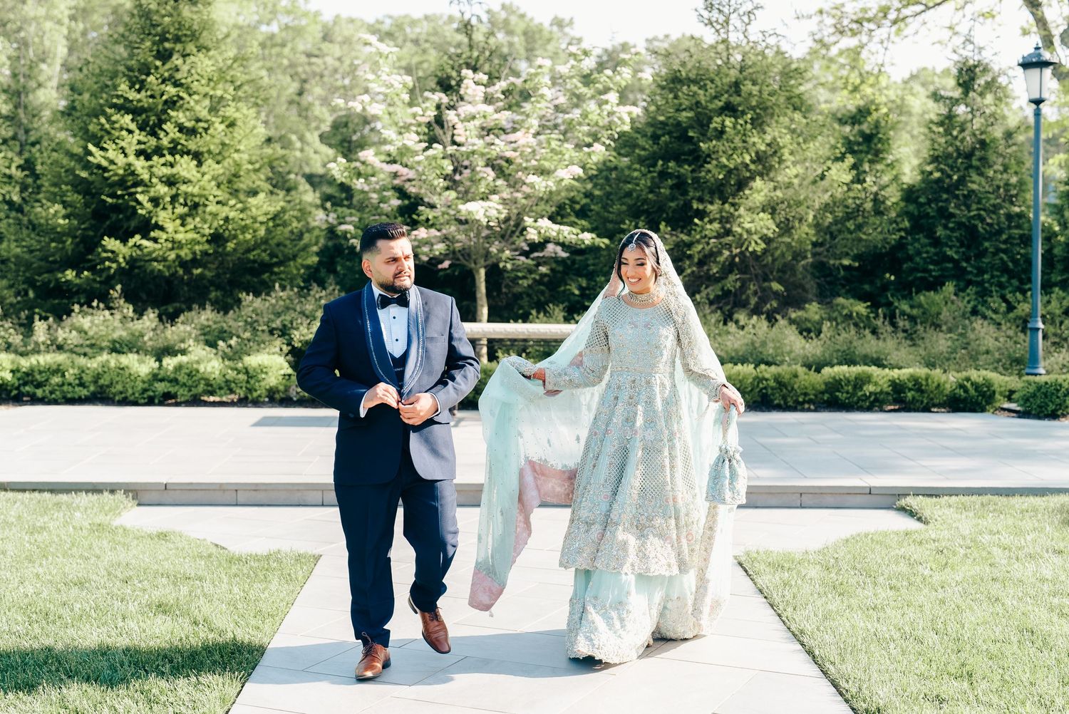 A couple walking together on a garden path, with the bride wearing a flowing white gown.