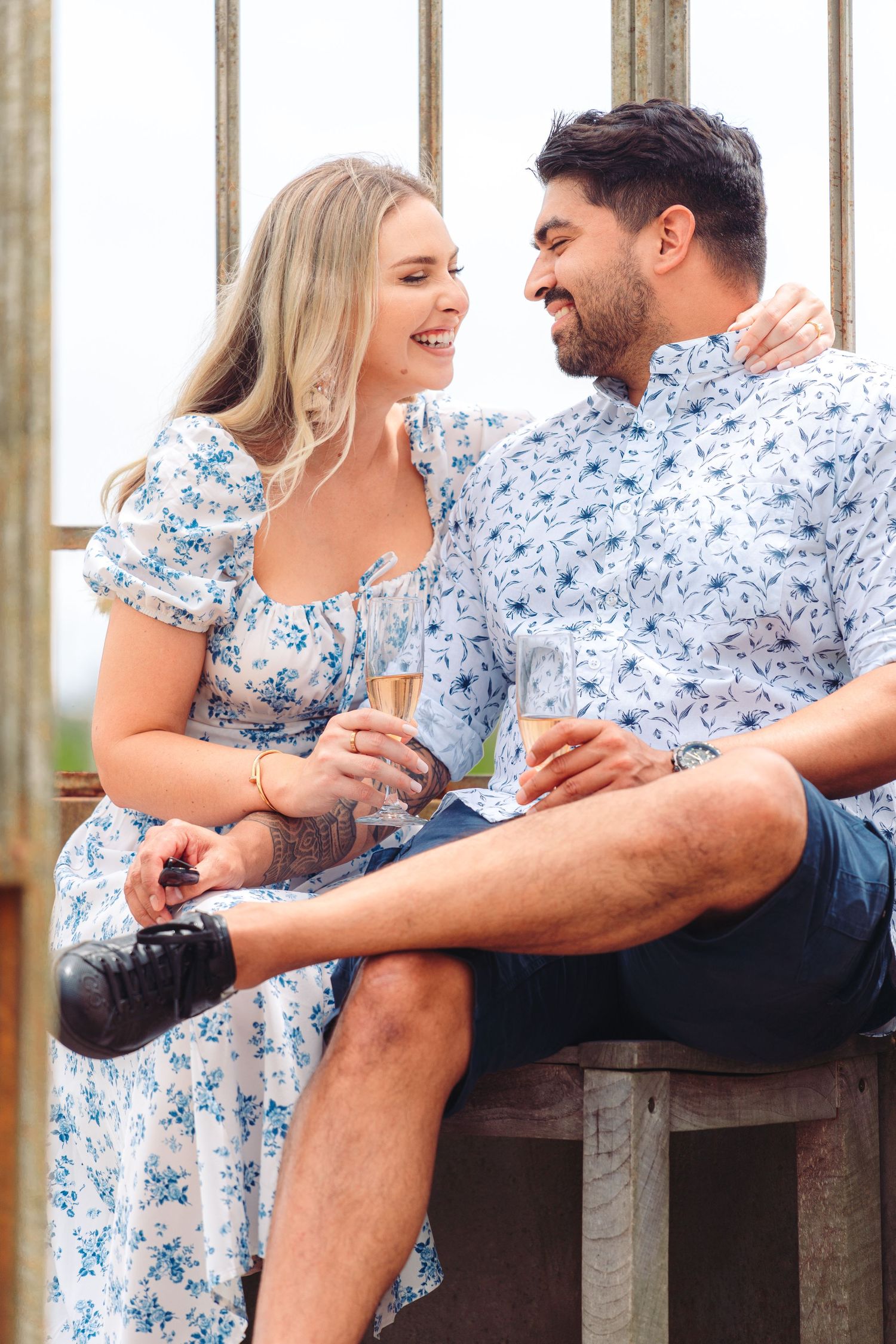 Couple wearing matching blue floral prints share a laugh while sitting together outdoors.