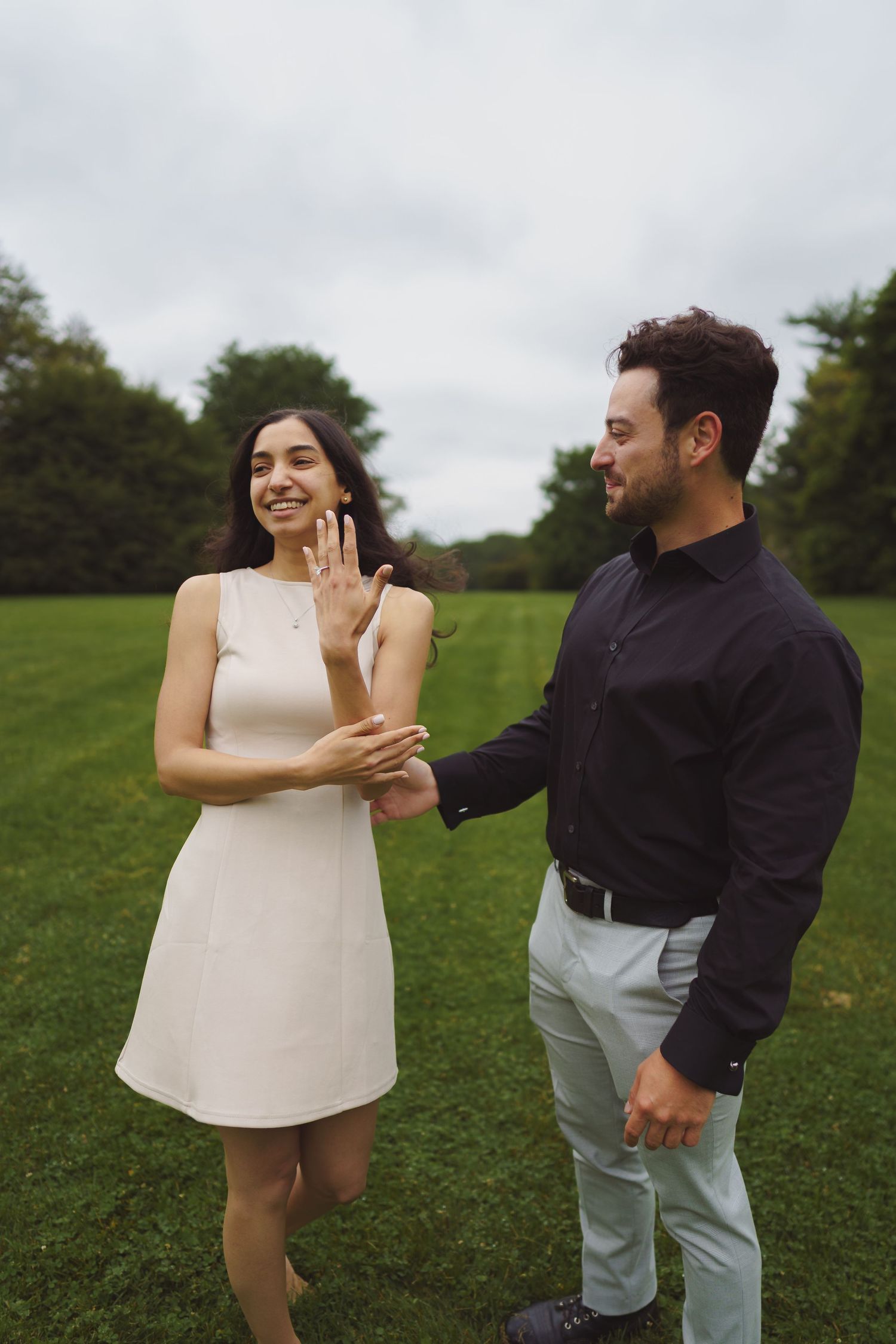 A couple laughing together in a grassy field as they admire something special on a cloudy day.