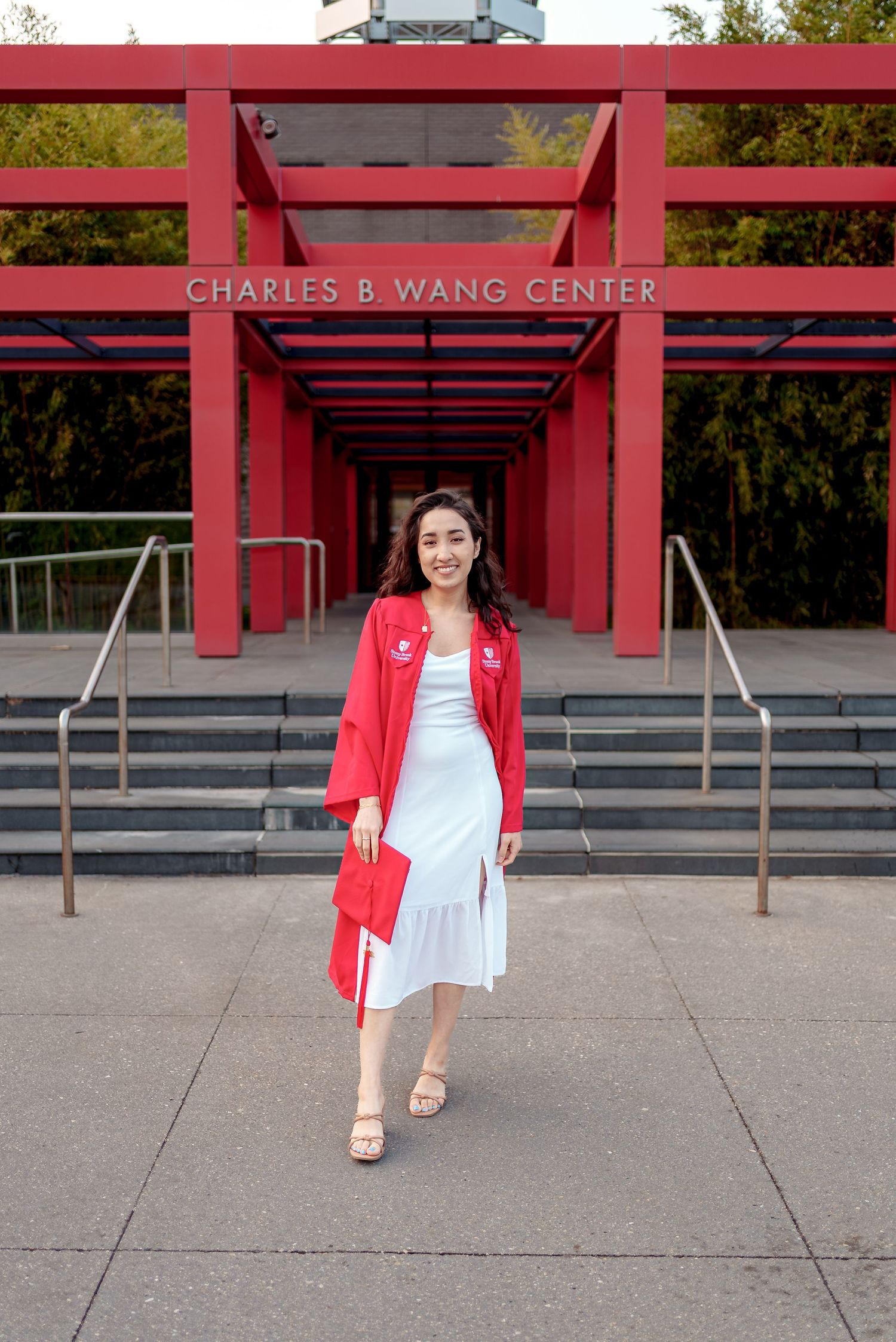 Someone stands in a red walkway entrance to the Charles B. Wang Center wearing a red blazer and white dress.