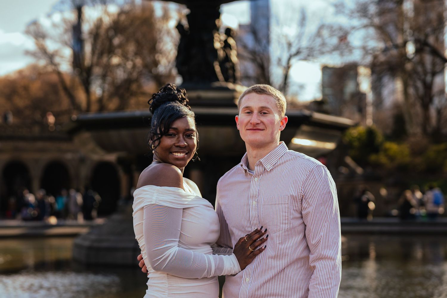 A couple in wedding attire pose together by a fountain in Central Park during golden hour.
