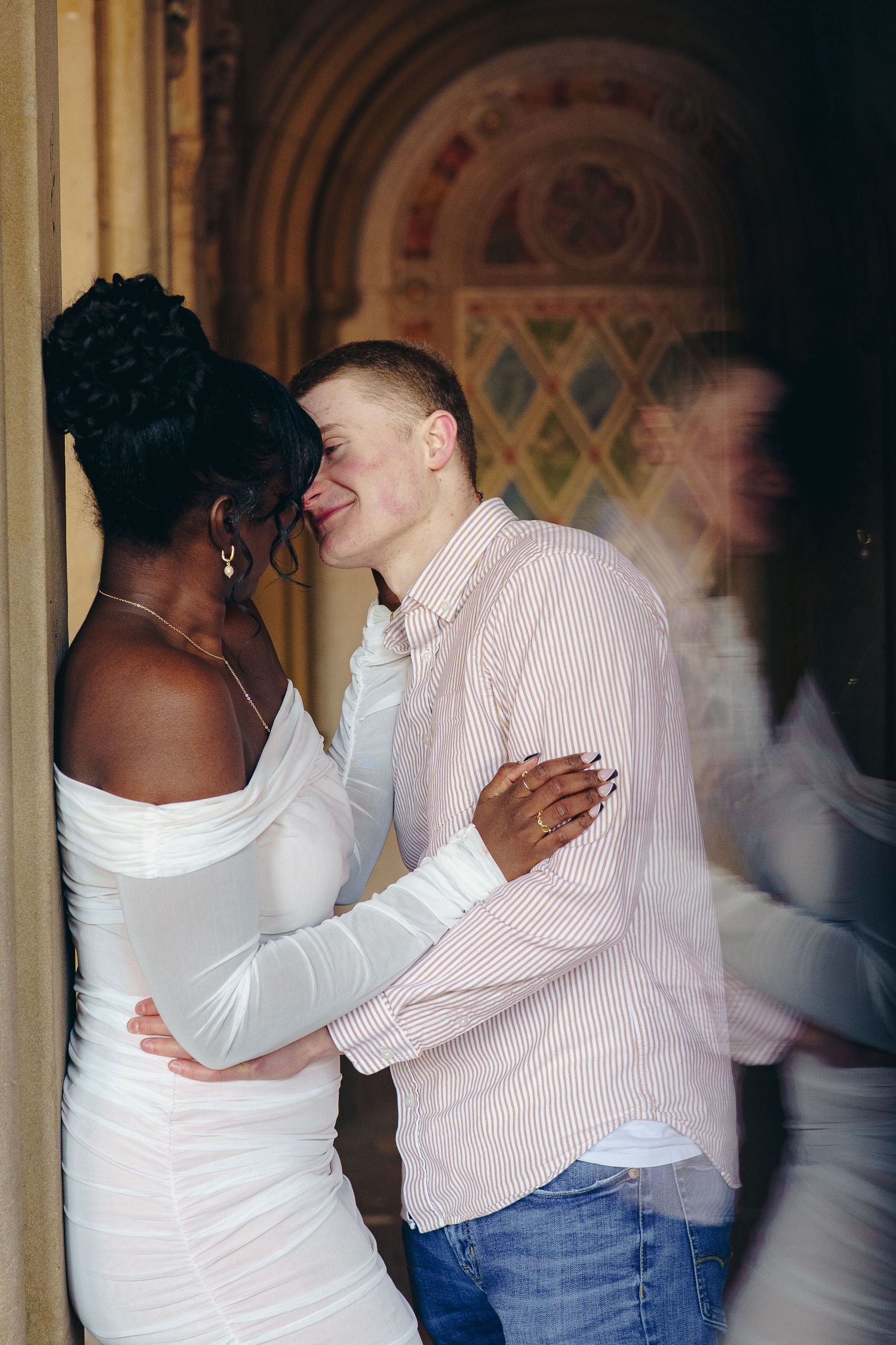 A couple shares an intimate moment together against an ornate archway background.