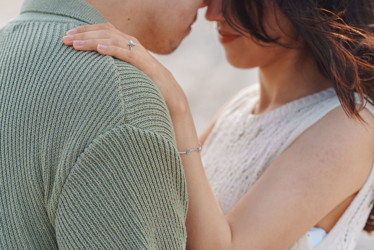 Two people share an intimate moment together wearing a green sweater and white lace top.