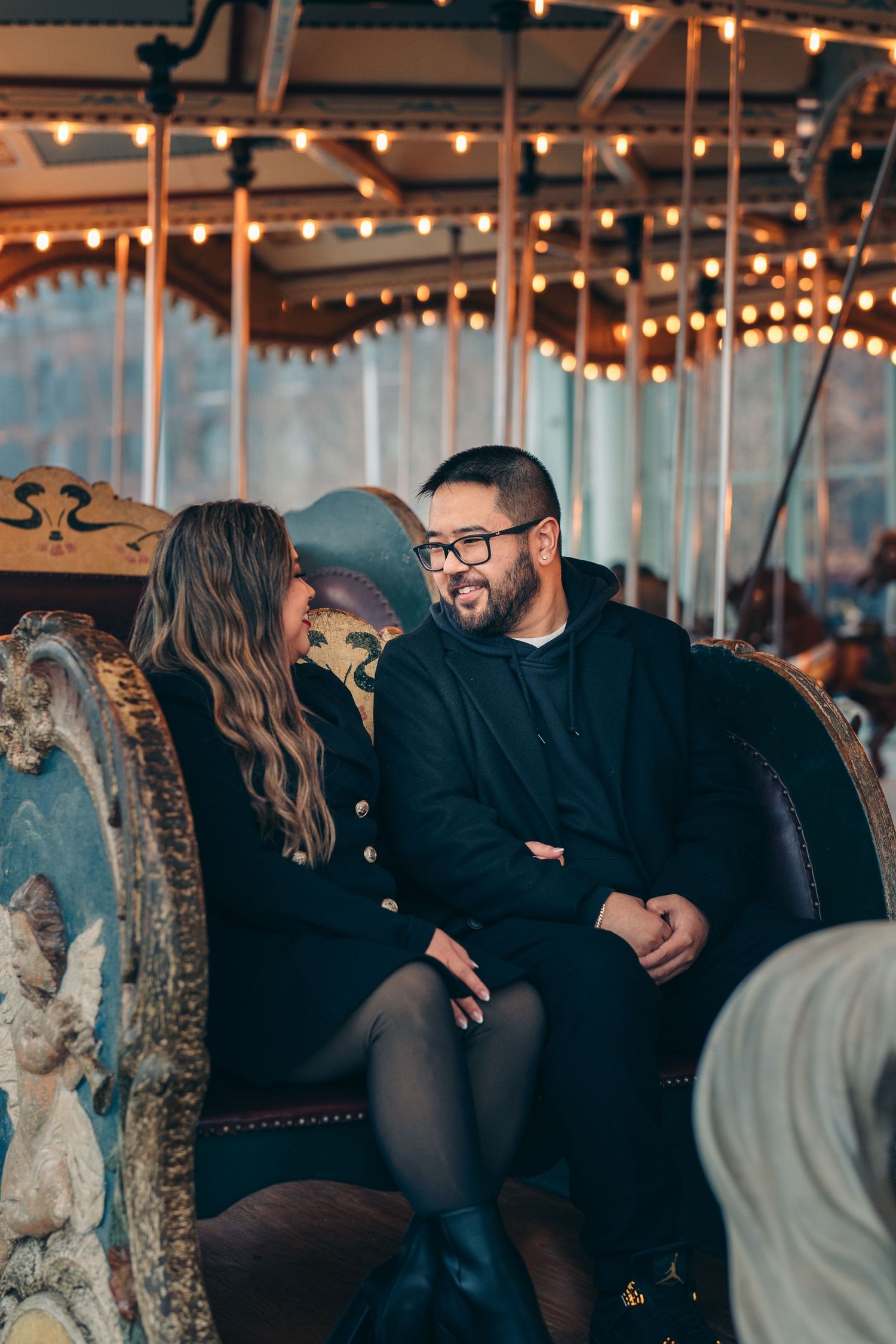 Couple sitting together on an illuminated carousel at night with glowing string lights creating a romantic atmosphere.