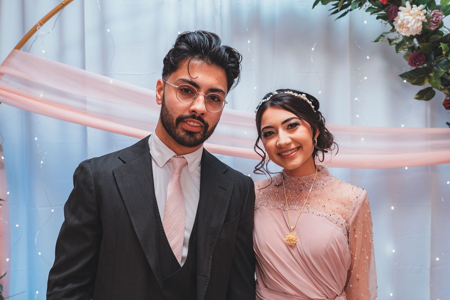 A couple poses together at an elegant celebration with pink decor and floral arrangements.