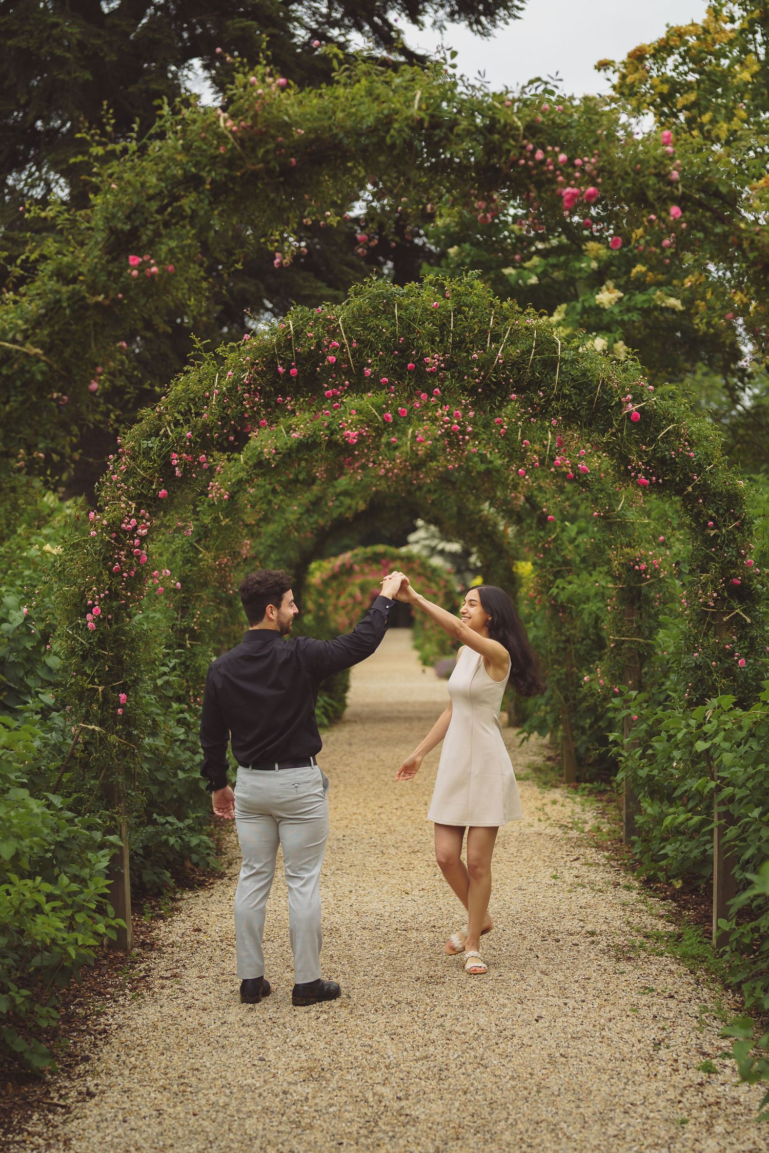 A couple dancing beneath a beautiful garden archway covered in pink climbing roses.