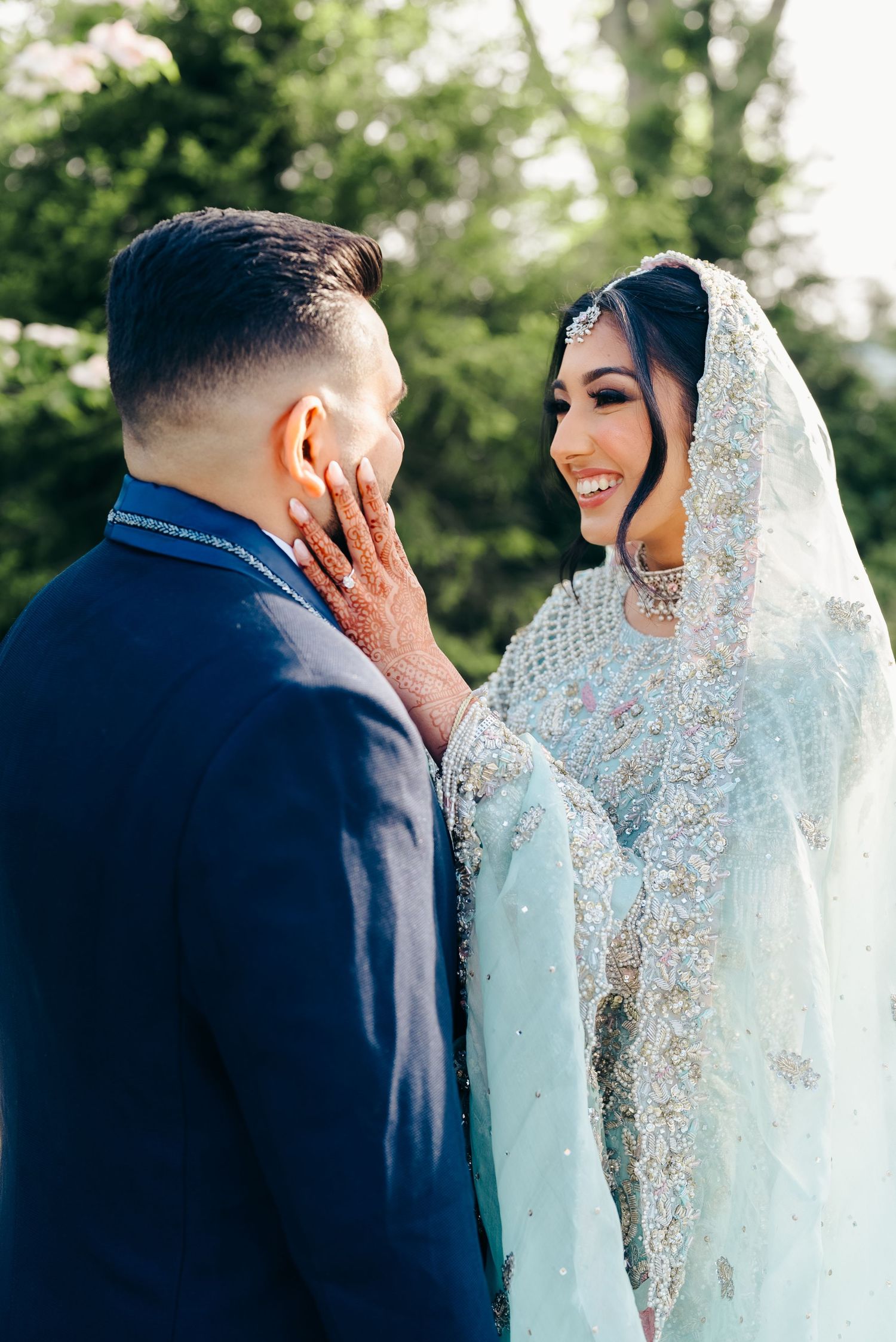 A joyful wedding moment captured outdoors with a bride in an elegant lace veil and groom in navy blue suit.