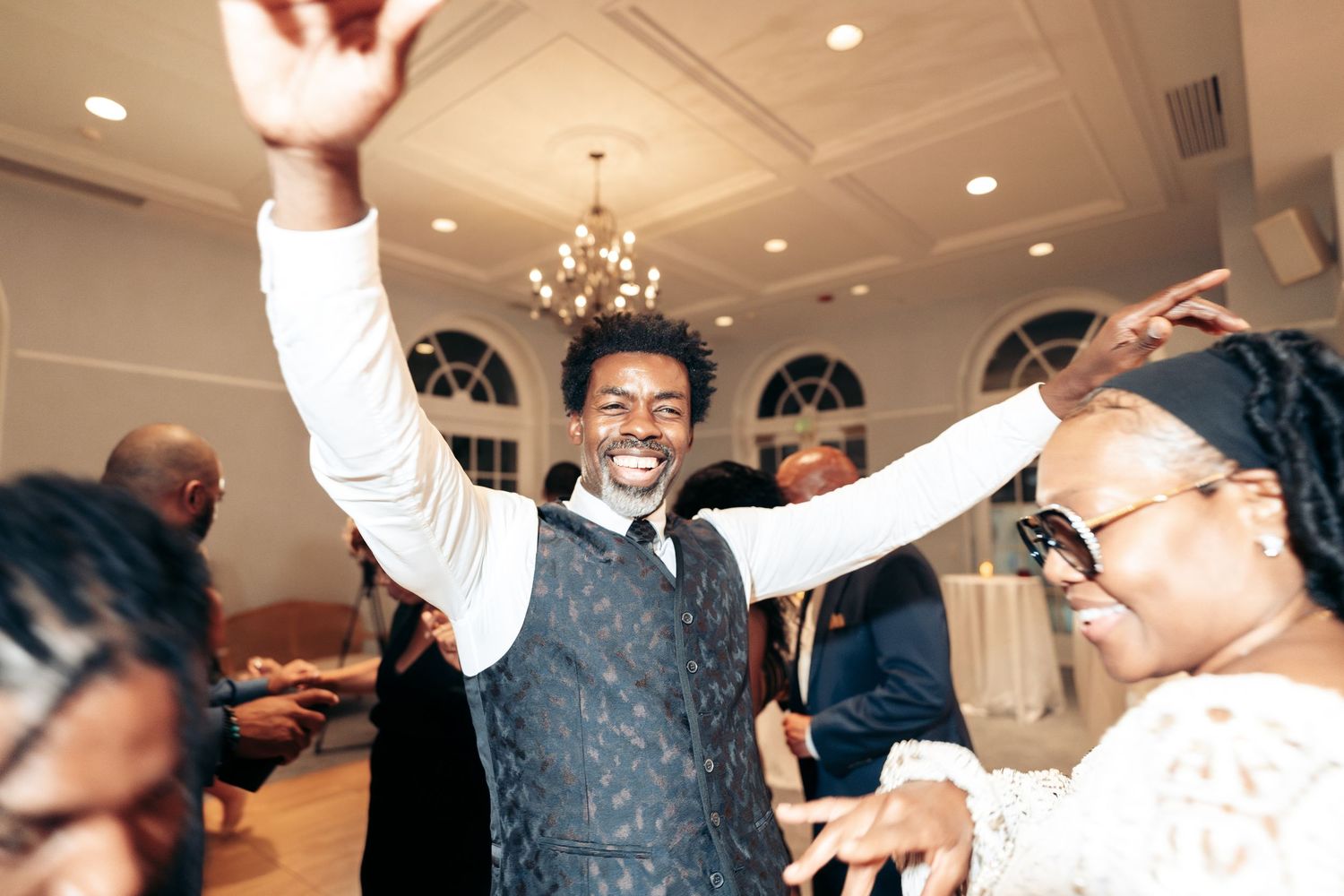People celebrating and dancing at a joyous formal event in an elegant room with a chandelier.