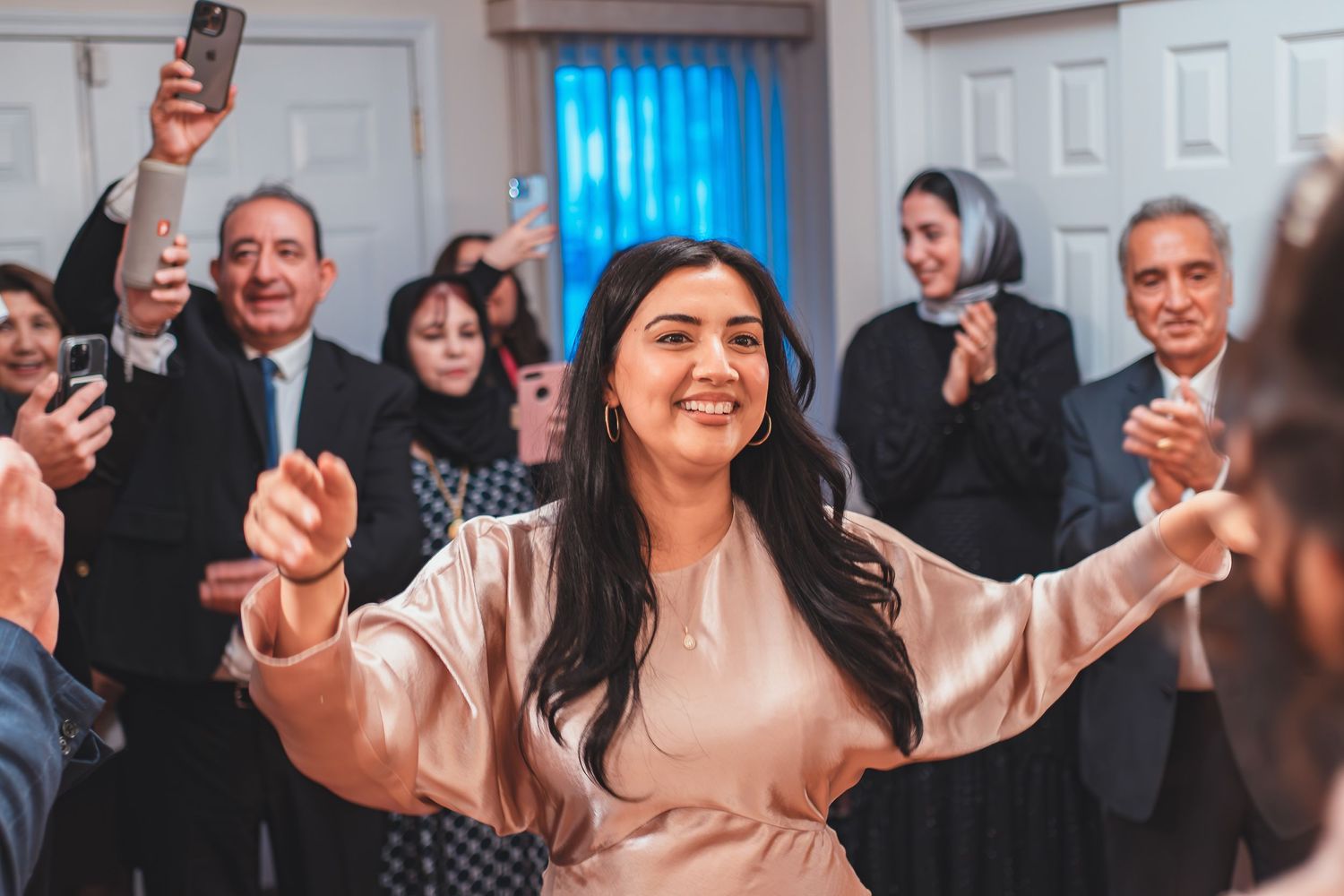 A celebration in progress with guests clapping and someone in pink celebrating with arms raised.