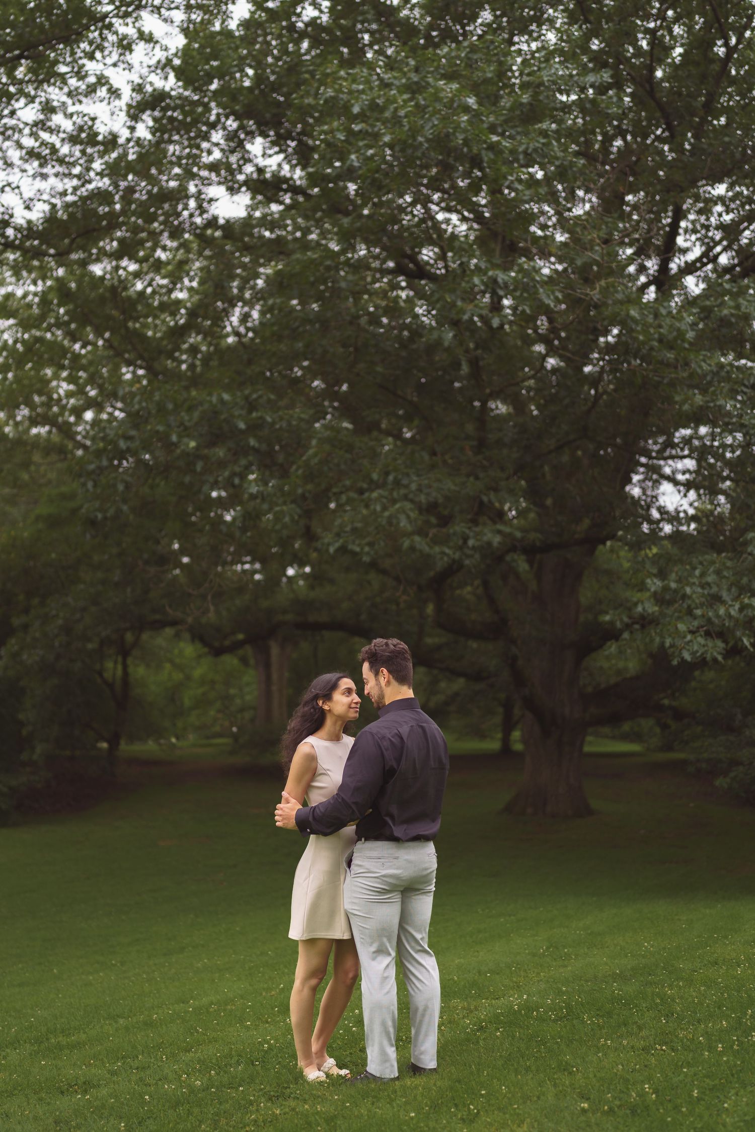A couple shares an intimate moment while walking together in a lush green park setting.