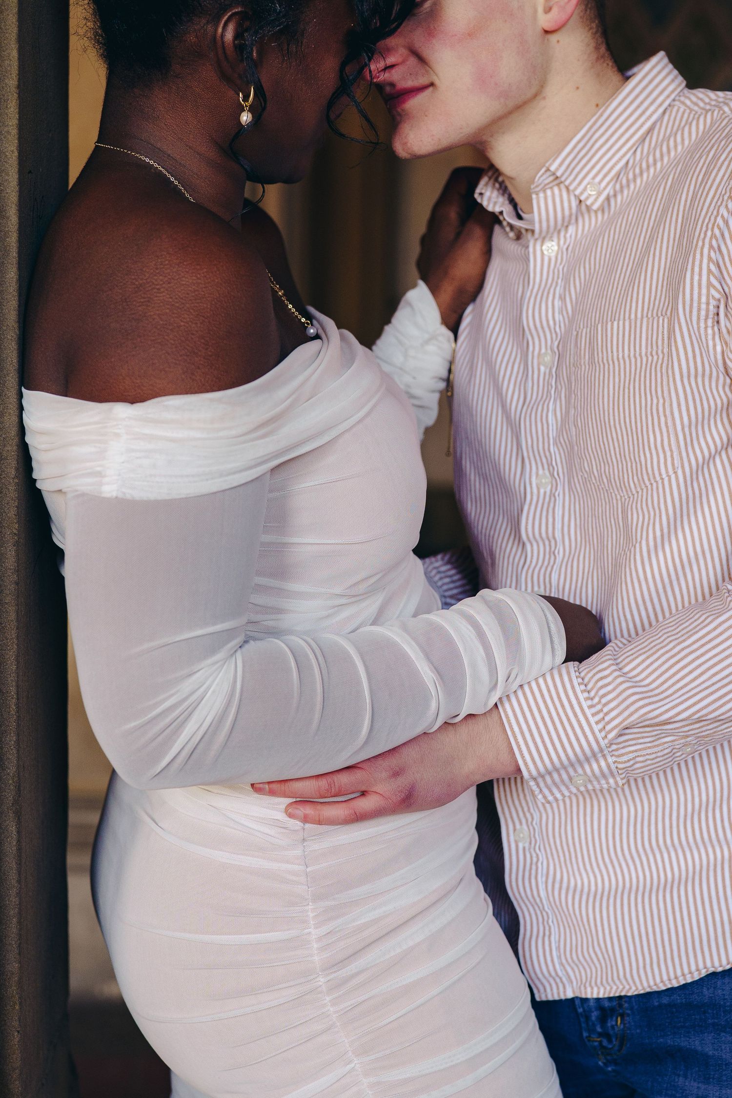 Two people in a tender embrace, one wearing a white dress with long sleeves and another in a striped shirt and jeans.