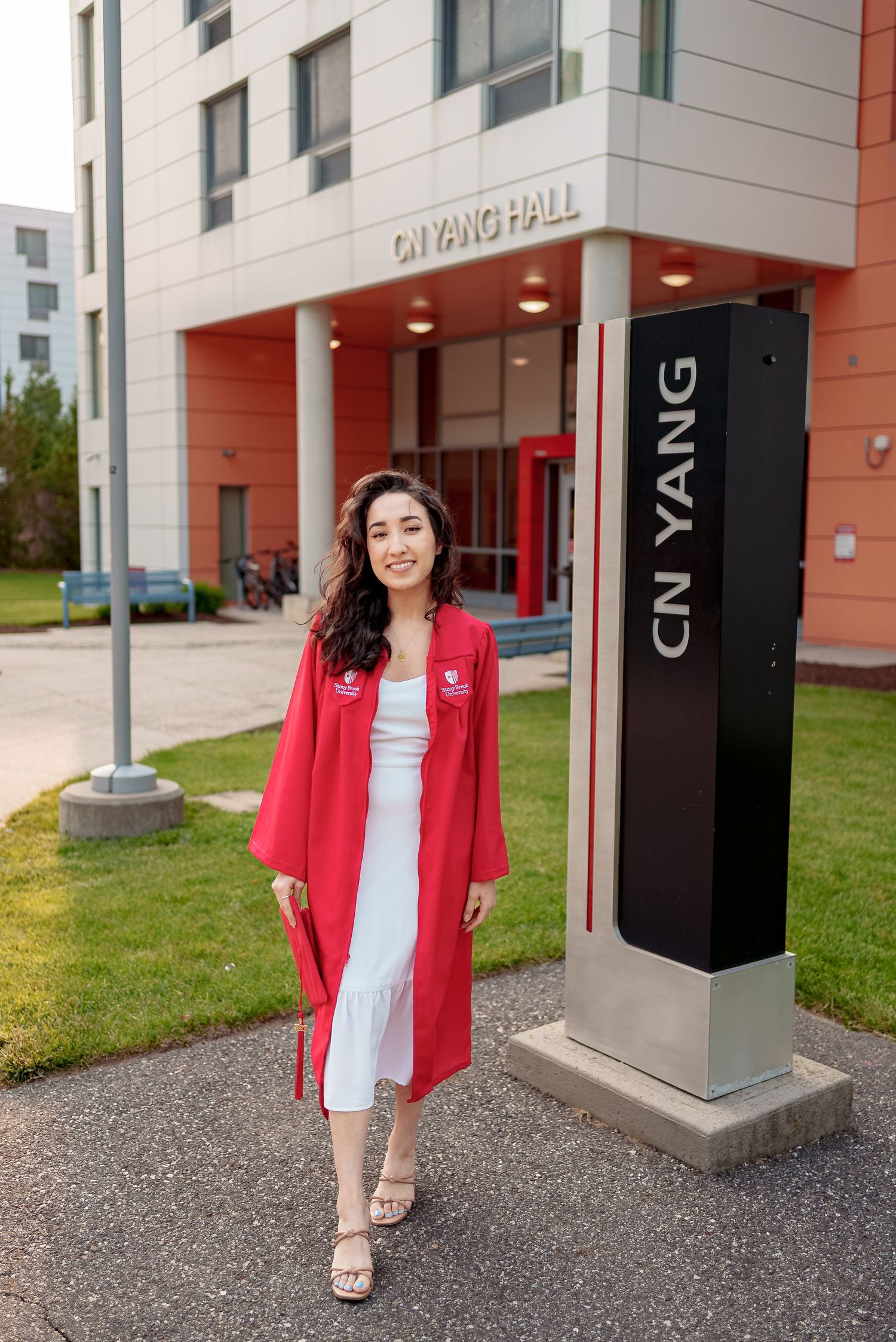 Graduate in red academic regalia stands in front of CN Yang Hall building entrance on campus.