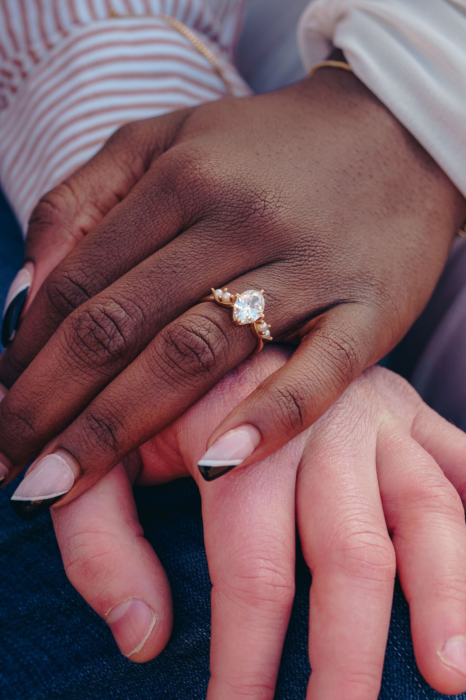 Two hands showcasing a beautiful diamond engagement ring, highlighting the contrast between skin tones and modern manicure.