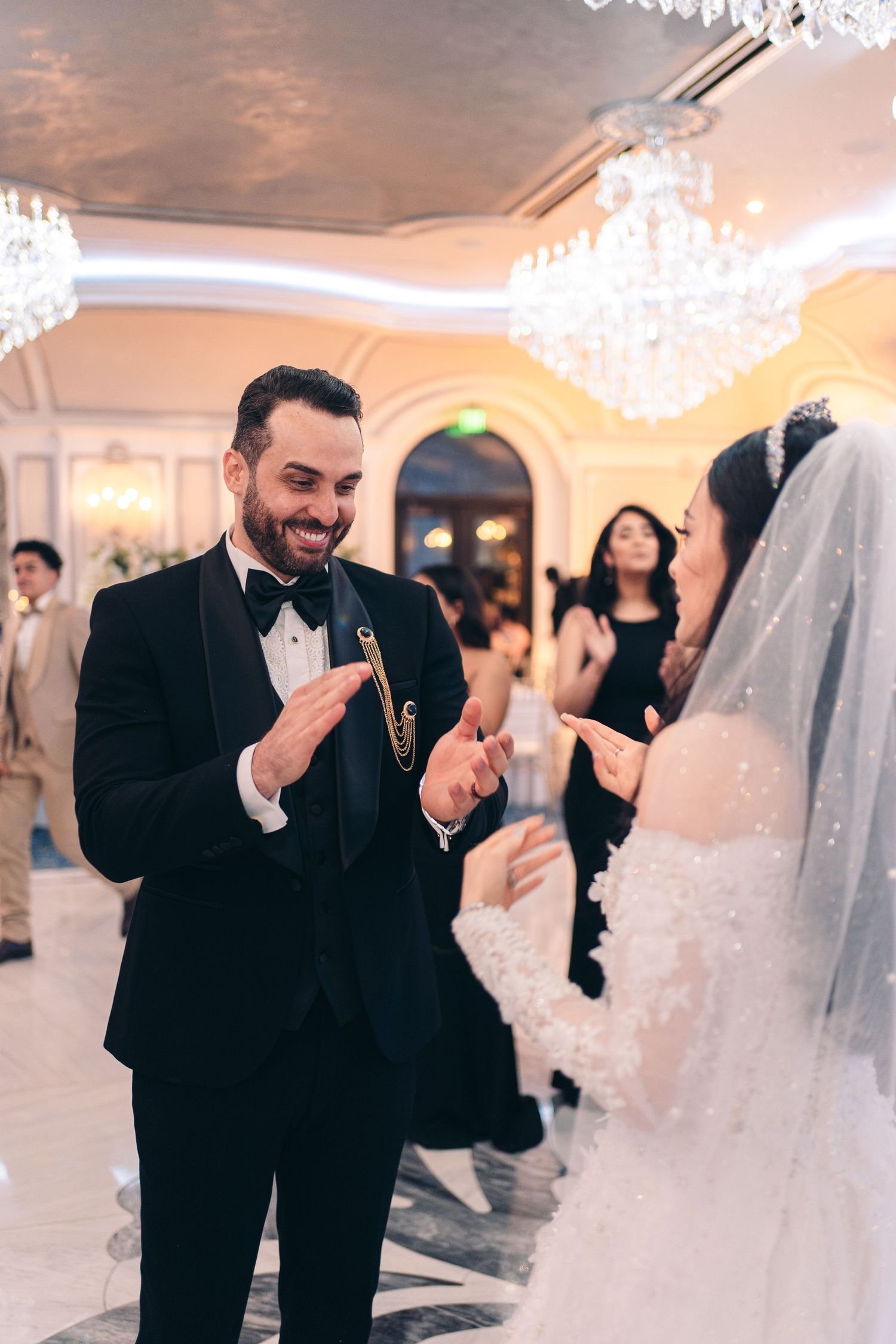A wedding celebration in an elegant ballroom with crystal chandeliers as the couple shares a joyful moment on the dance floor.