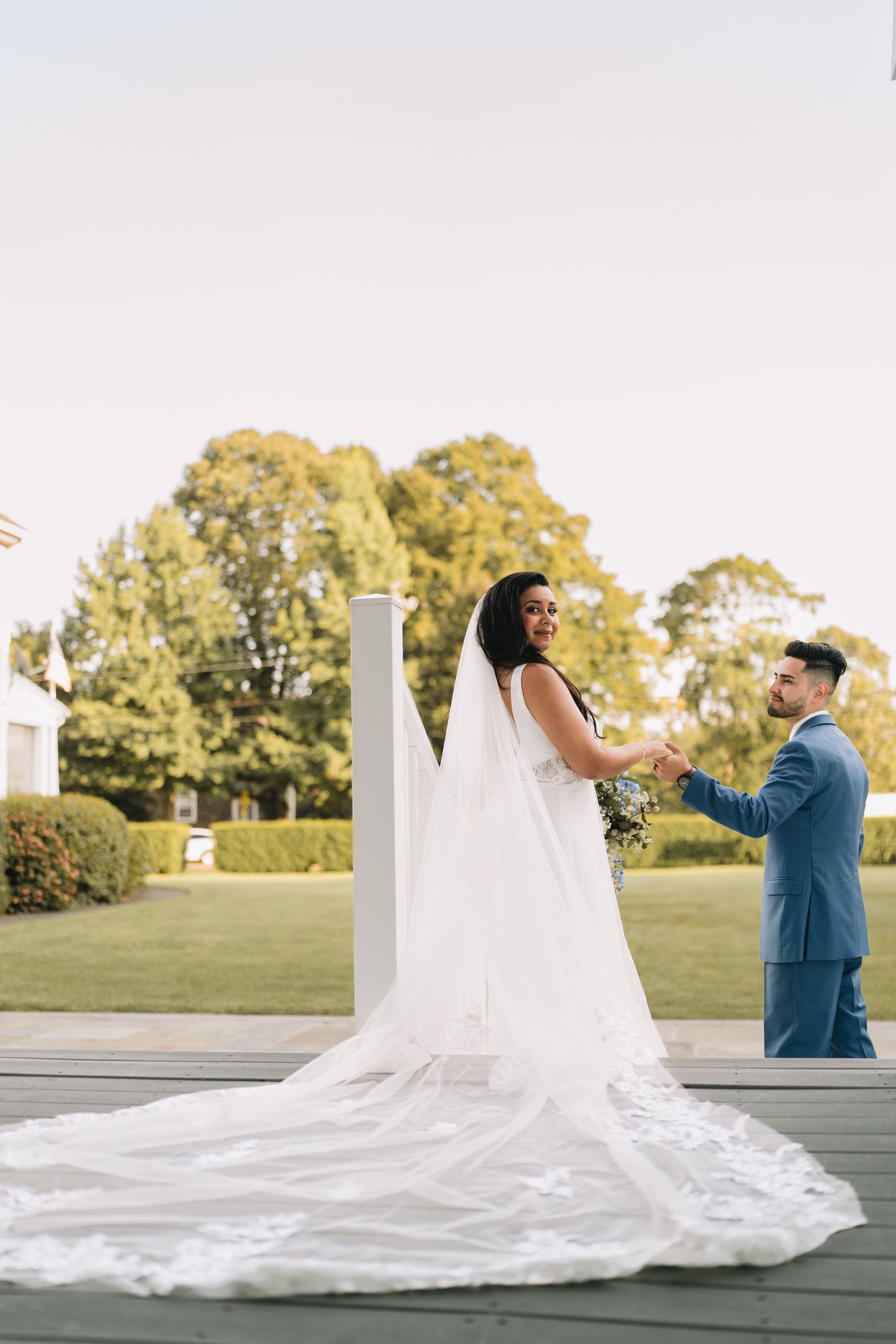 A couple shares a romantic moment on a deck, with the bride wearing a stunning white gown with a flowing cathedral train.