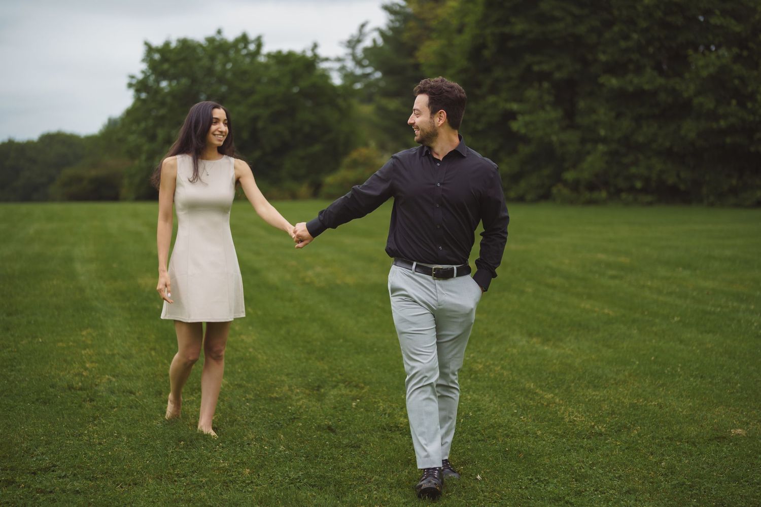 A couple holds hands while walking together on a lush green lawn in summer.