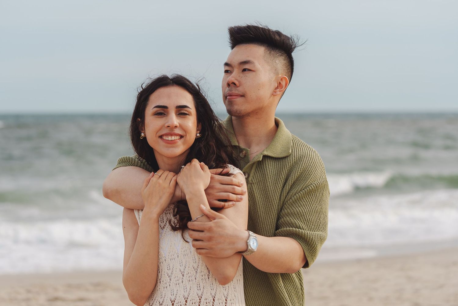 A couple shares a romantic moment together while embracing on a sandy beach with ocean waves in the background.