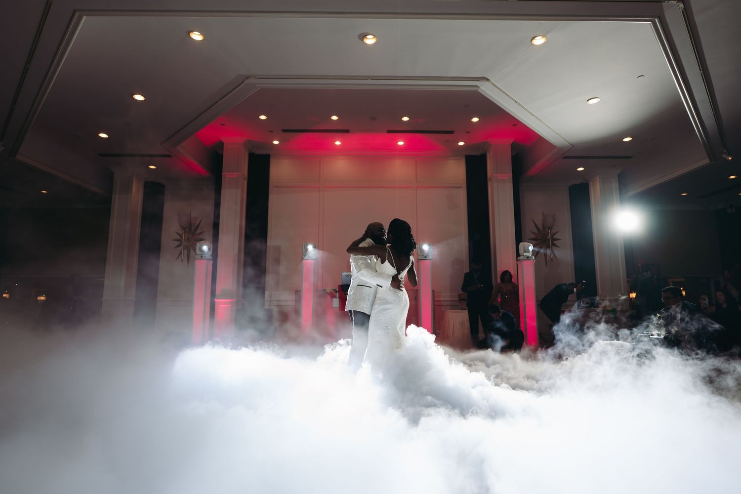 A couple shares their first dance on a foggy dance floor with dramatic red uplighting at their wedding reception.