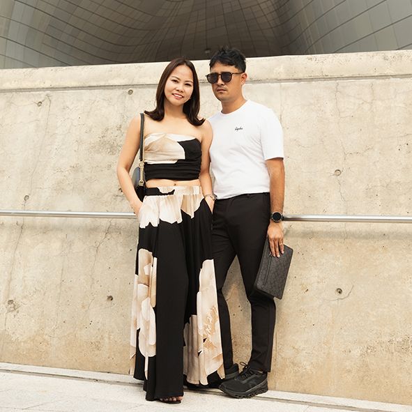 Stylish couple in coordinated black and white outfits pose against a concrete wall in an urban setting.